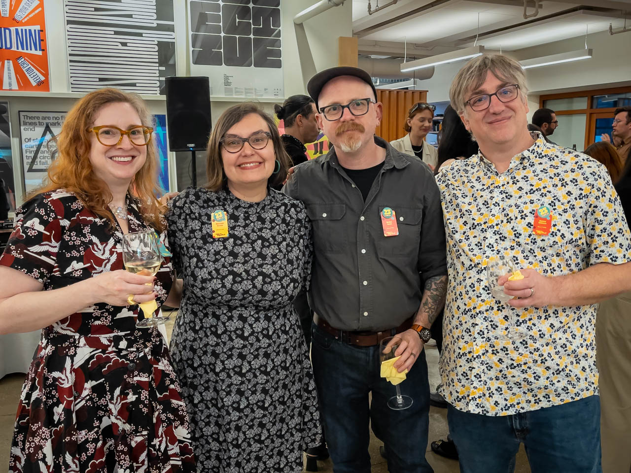 four people at a cocktail party looking at the camera holding wine glasses