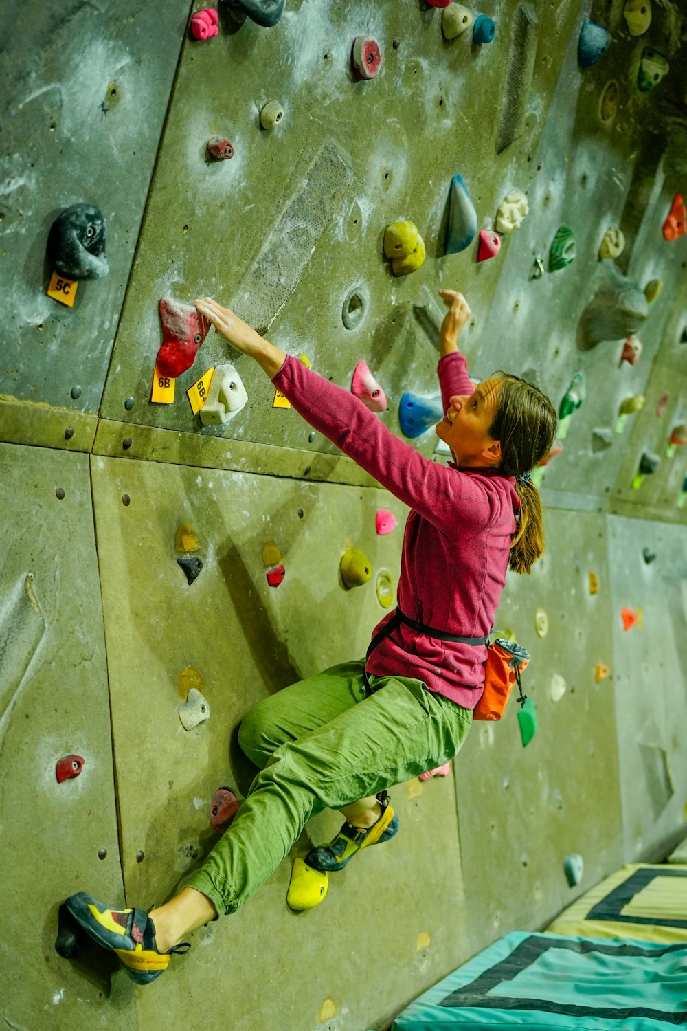 A girl in a pink shirt reaches across a green wall full of holds