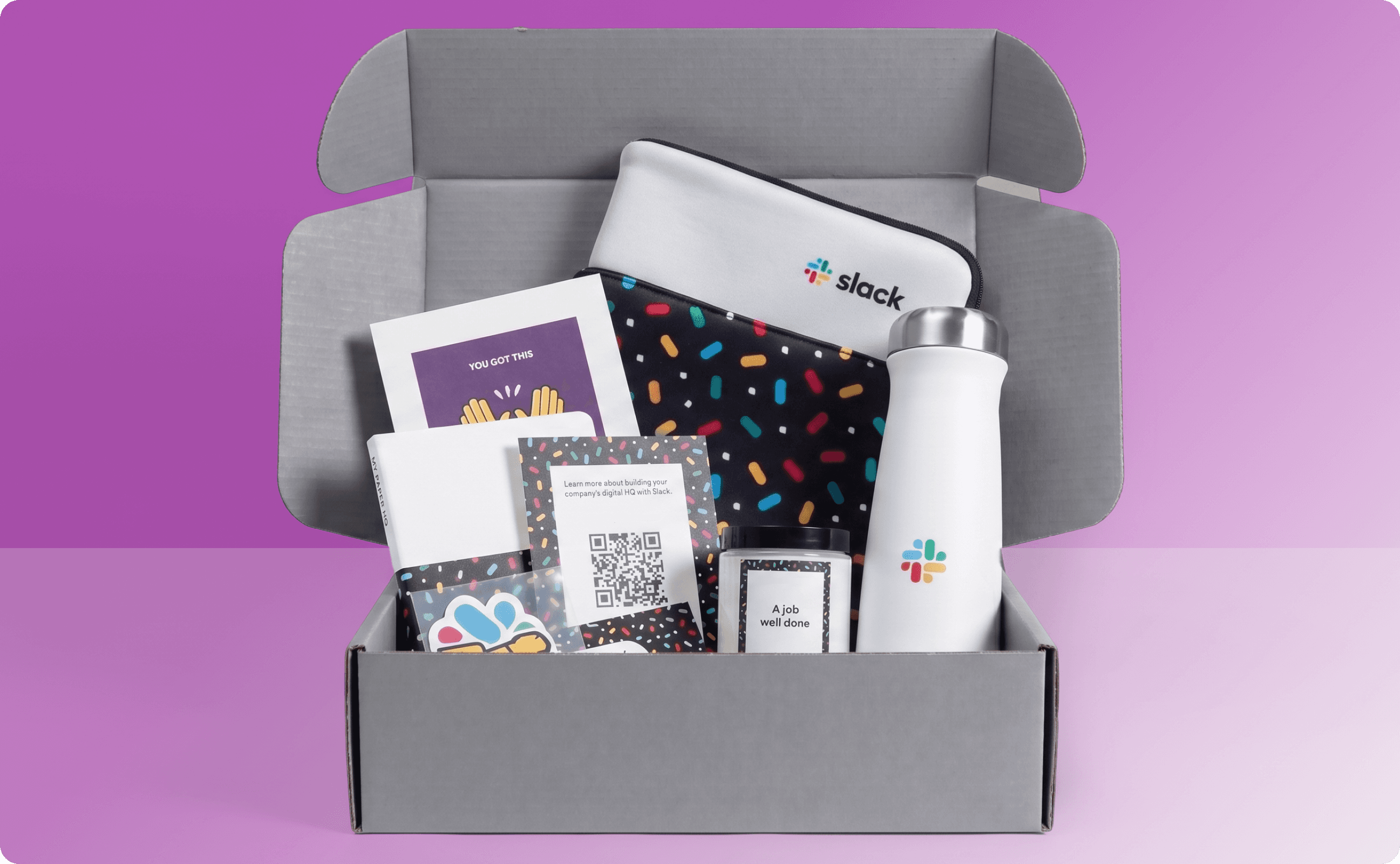 Slack's new hire swag kit containing a notebook, a laptop sleeve, a candle, and a tumbler.