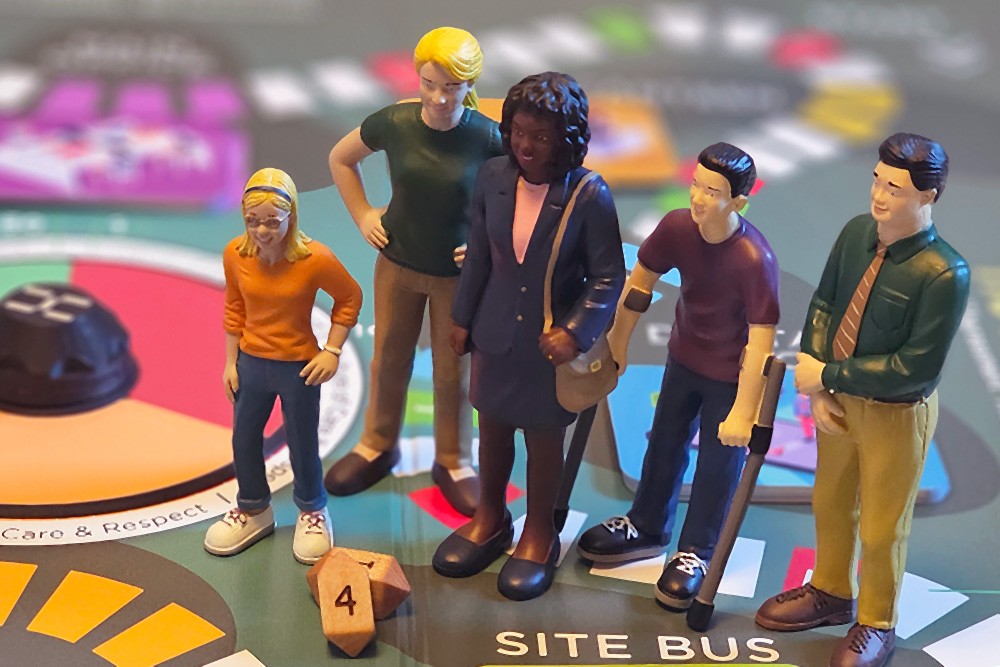 Five diverse miniature character figurines standing on the "Site Bus" square of a colourful workplace-themed board game.