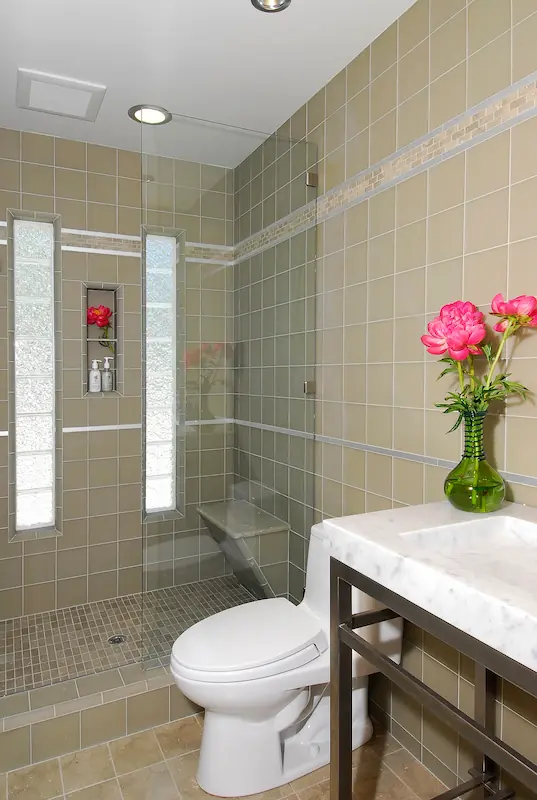 Neutral-toned full bathroom with tiled walls, glass shower, and fresh flowers. Irvine Transitional Modern. Photo by Chris Darnall.