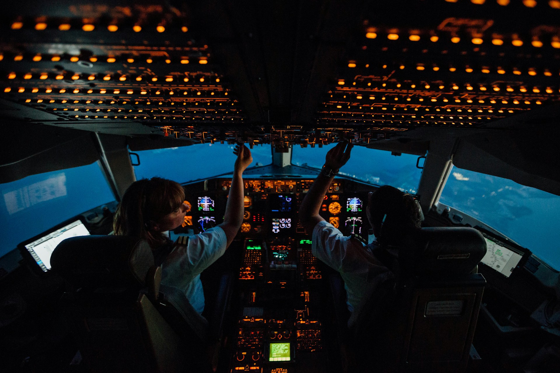 A widescreen perspective of an aircraft cockpit with two pilots operating