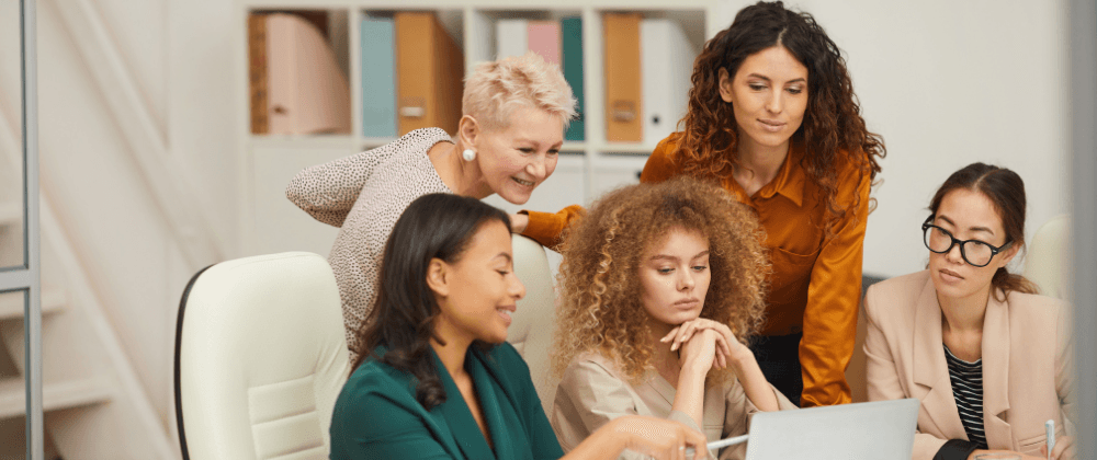 Five women huddled over a laptop at work