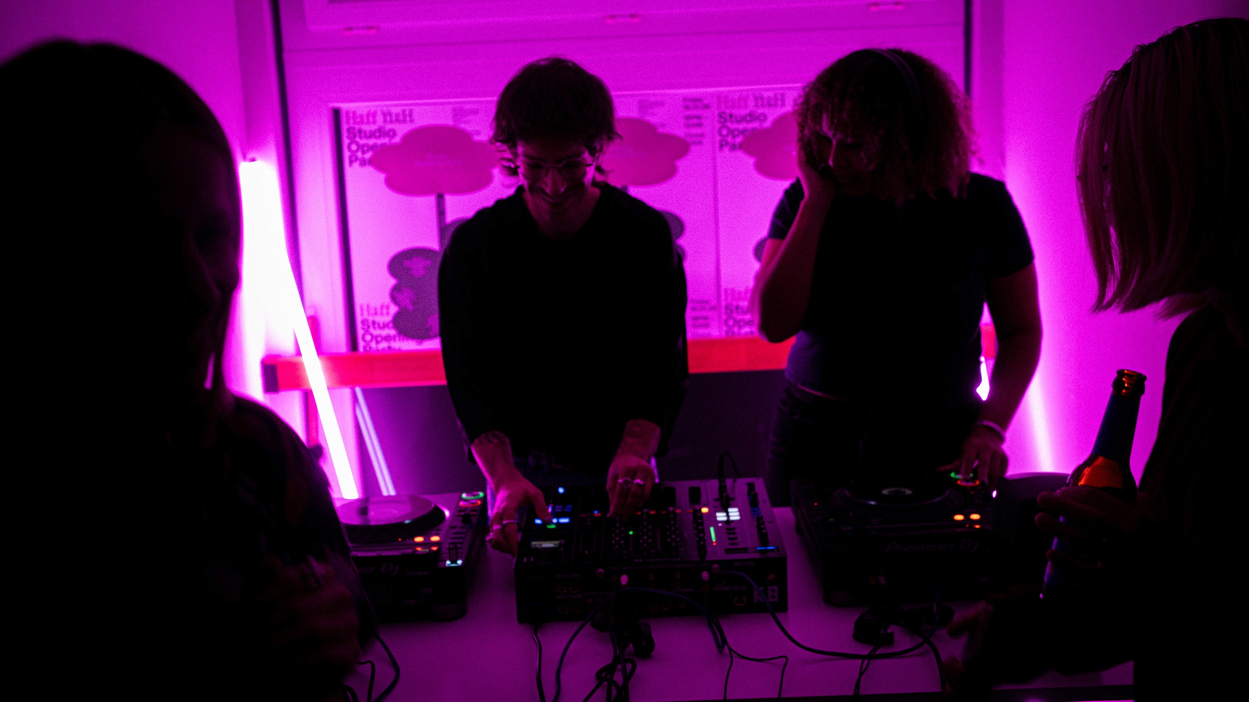 A vibrant, purple-lit scene of a DJ duo performing at the studio's housewarming event. The image captures the energetic atmosphere of the opening party, showcasing the studio's engagement with the local creative community and immersive event curation.