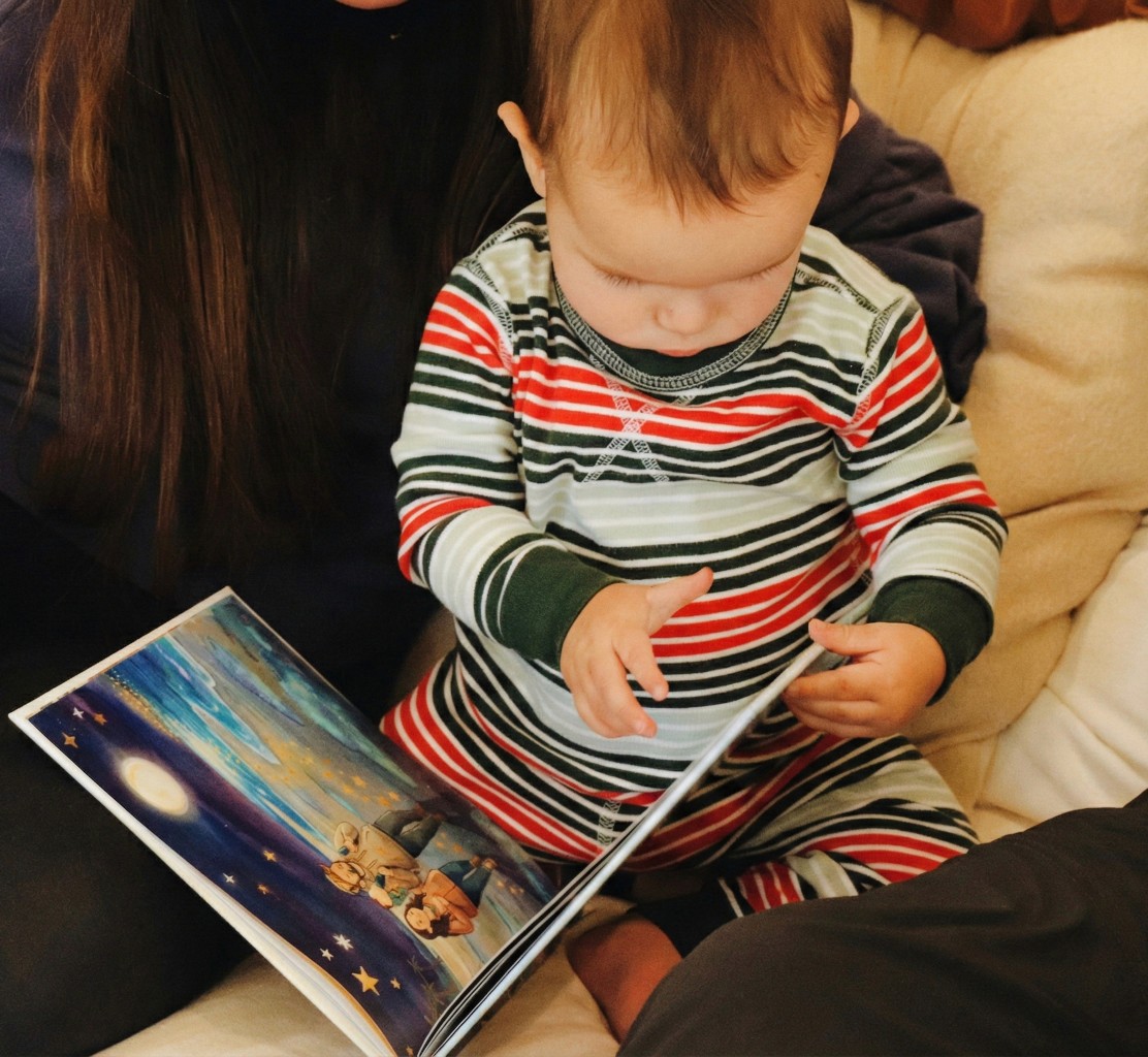 Smiling young woman with long hair standing against a dark green background, holding a finger to her chin.