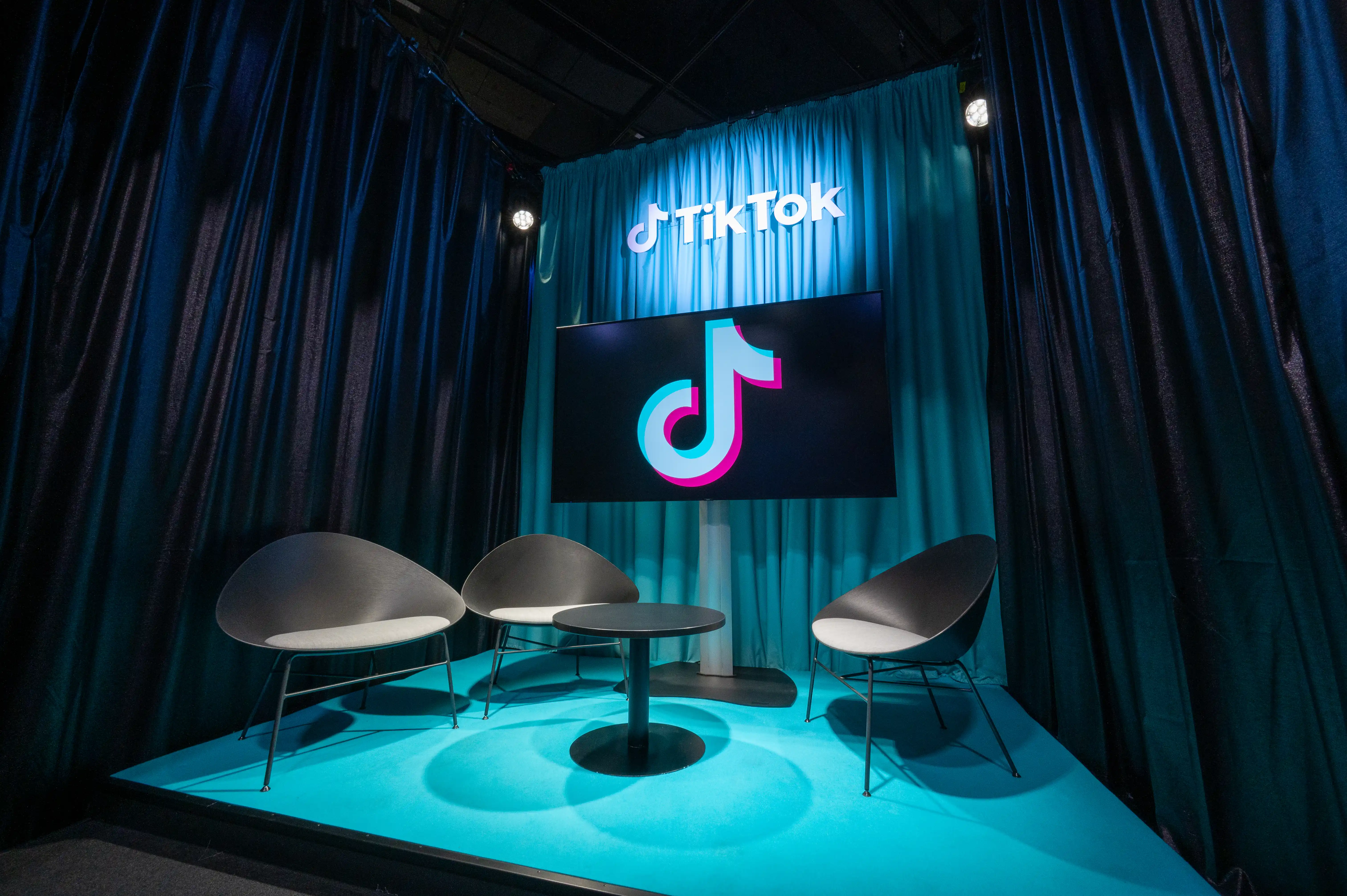 Turquoise-lit interview corner with cone chairs and TikTok screen in front of shimmering curtains at Gamescom.