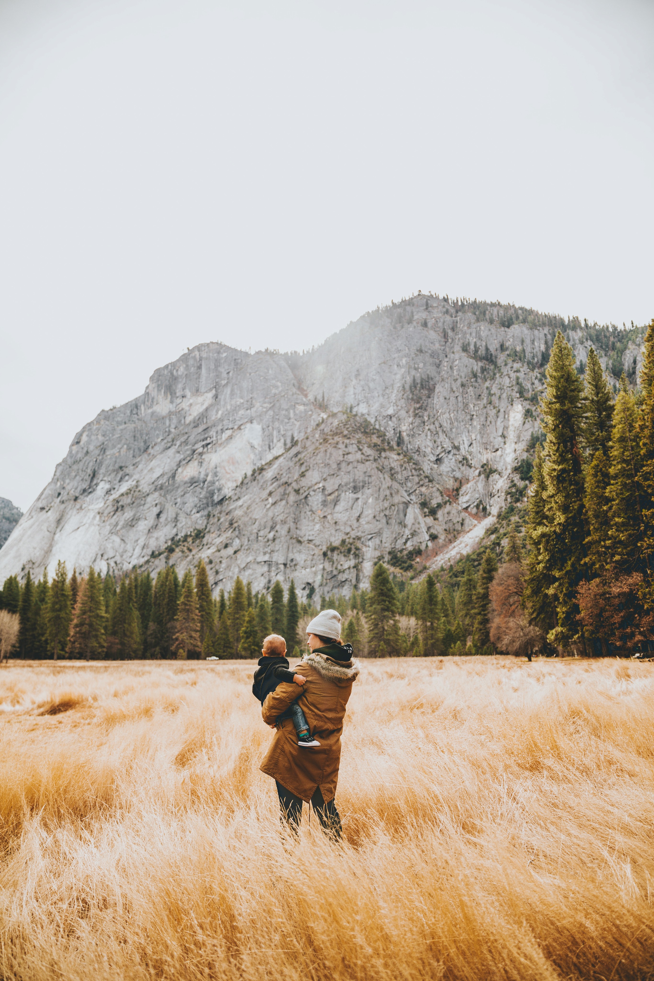 a girl with a boy standing on a field looking at a mountain in the far