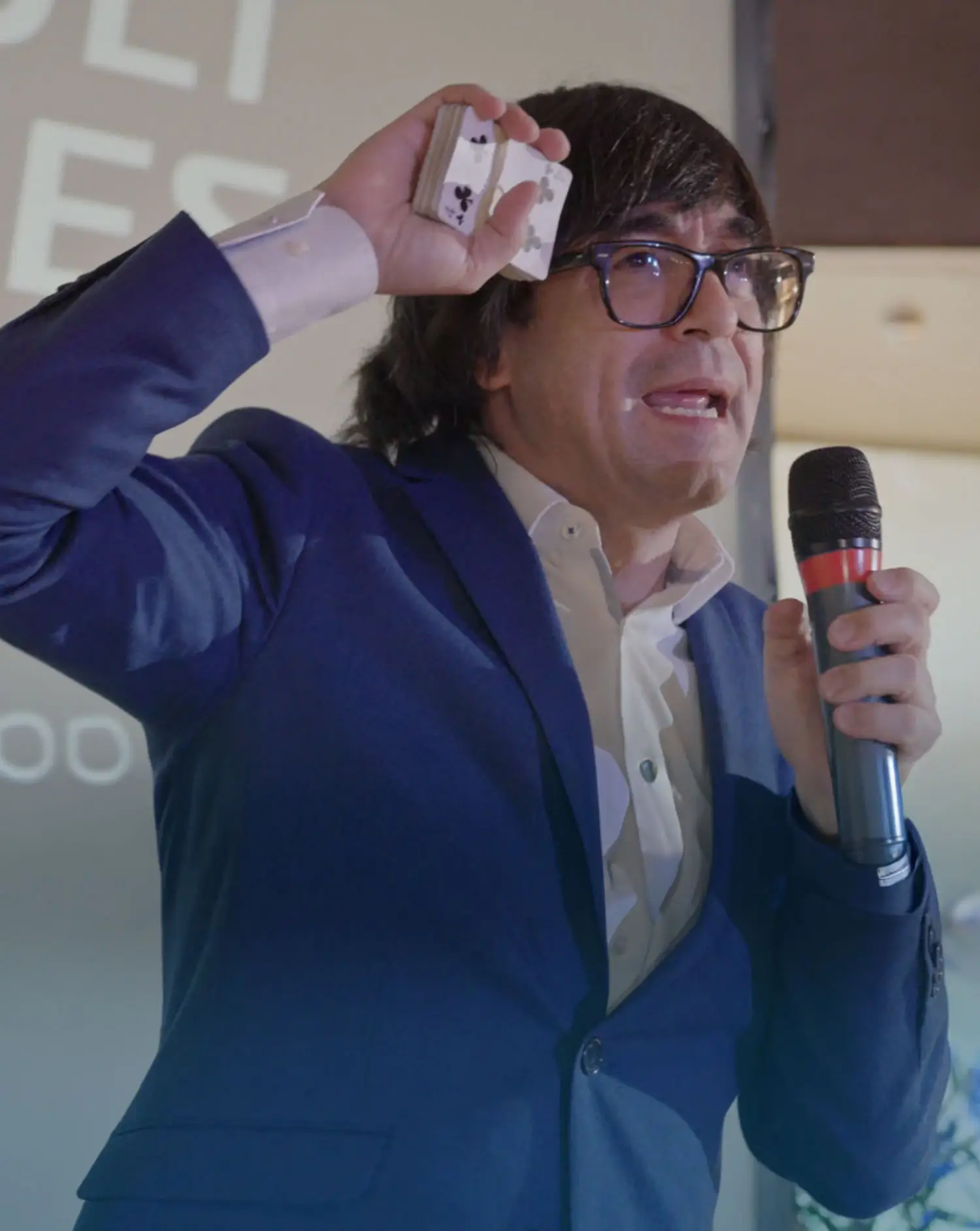 Portfolio Thankium: Hombre con traje azul realizando truco de magia con cartas y micrófono en mano.
