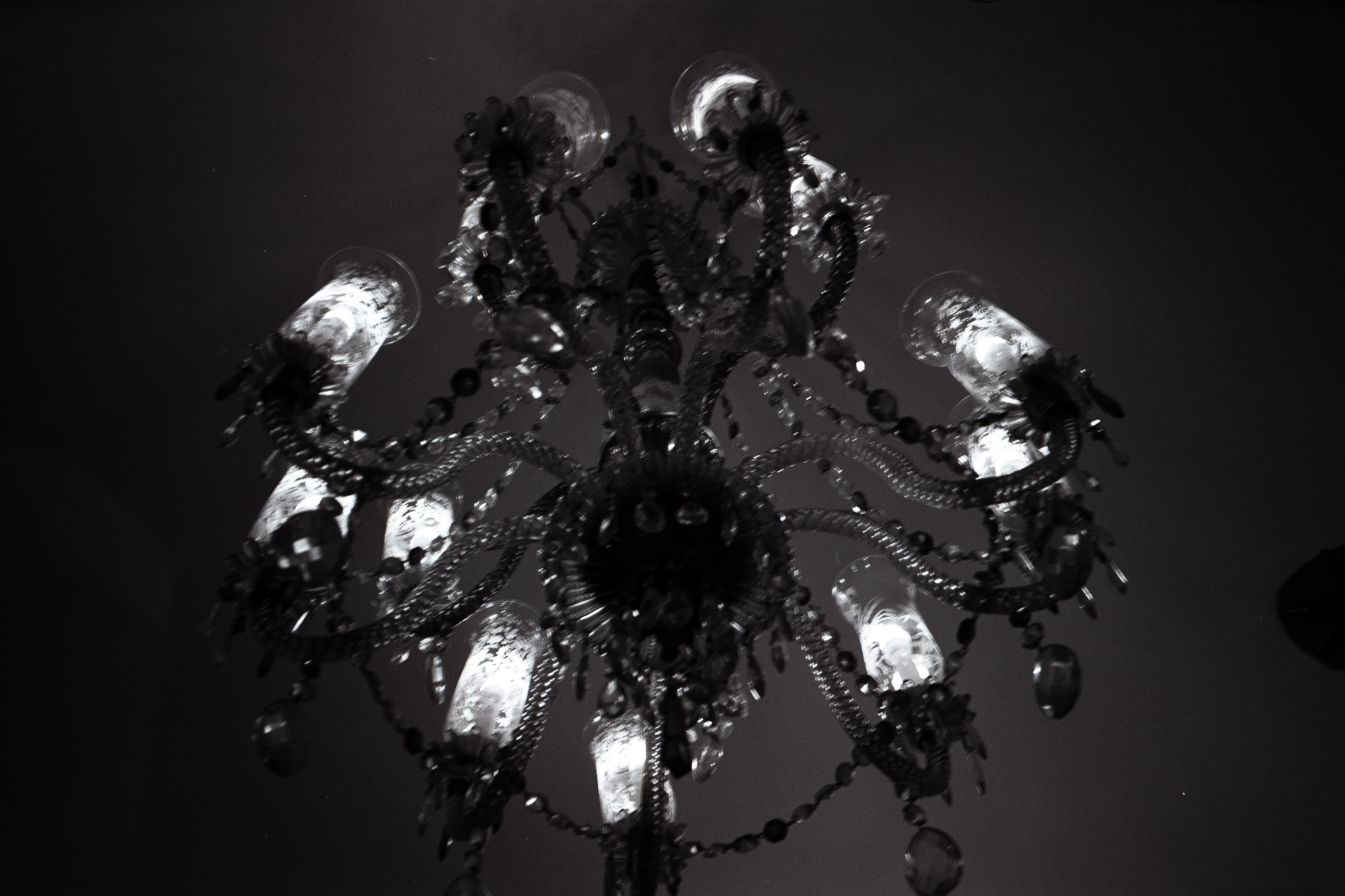 A vintage, ornate chandelier with multiple intricate glass arms and bulbs illuminates softly in a dark room, casting elegant shadows.