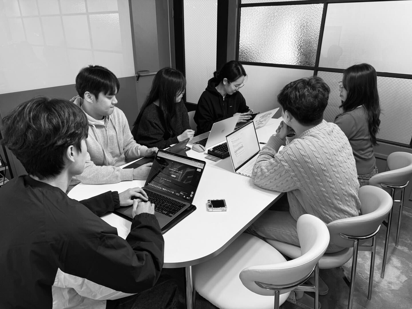 Black and white photo of two people looking at a computer screen with papers on wall