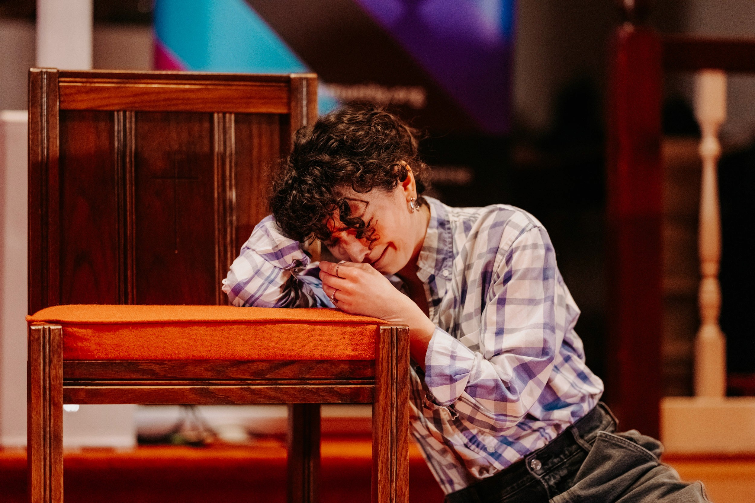 Performer in an emotional moment leaning against a chair during the Queer Open Mic (QOM) hosted by be; community in Bridgewater, Massachusetts