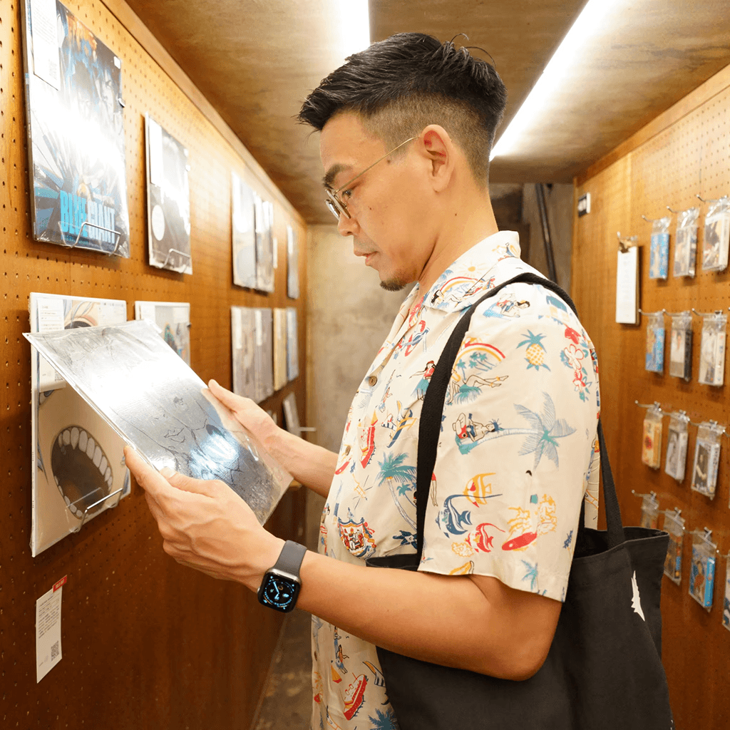 A male person with hawaiian shirt looking at the cover of a vinyl record on his hands