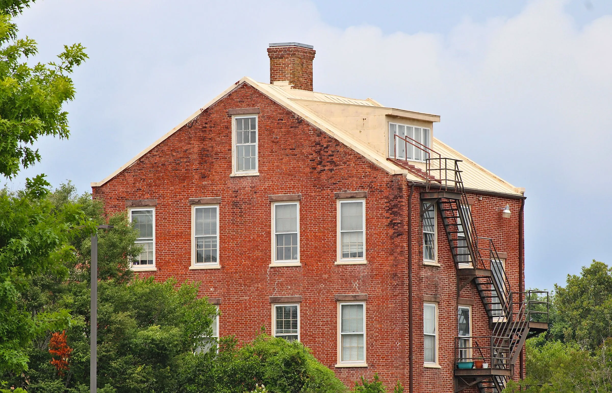 Red brick building with a black fire escape among green trees