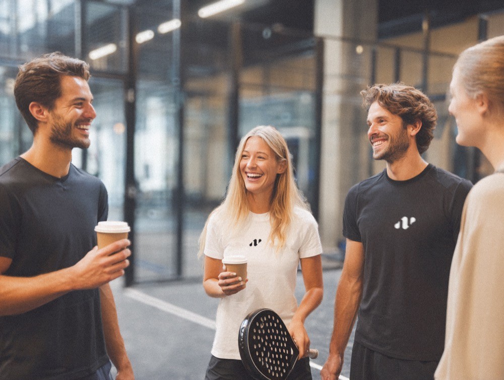 Gruppe junger Padelspieler lacht und unterhält sich nach dem Match auf dem Court