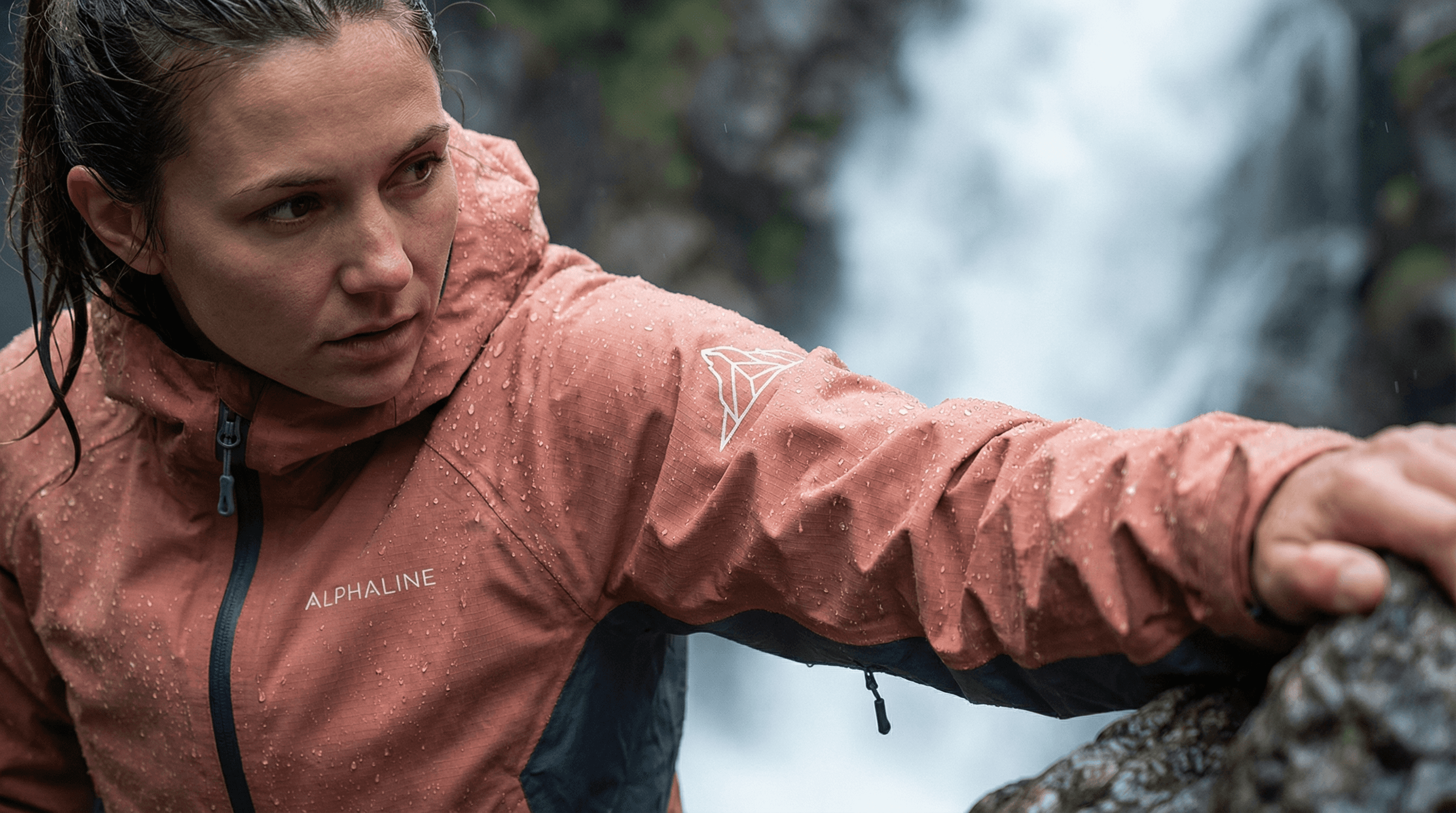 Woman wearing an ALPHALINE alpine jacket while climbing near a waterfall