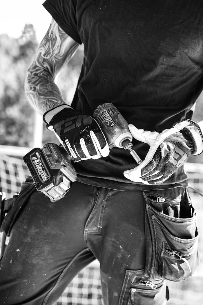 A black and white photo of a man wearing gloves holding a cordless impact wrentch.