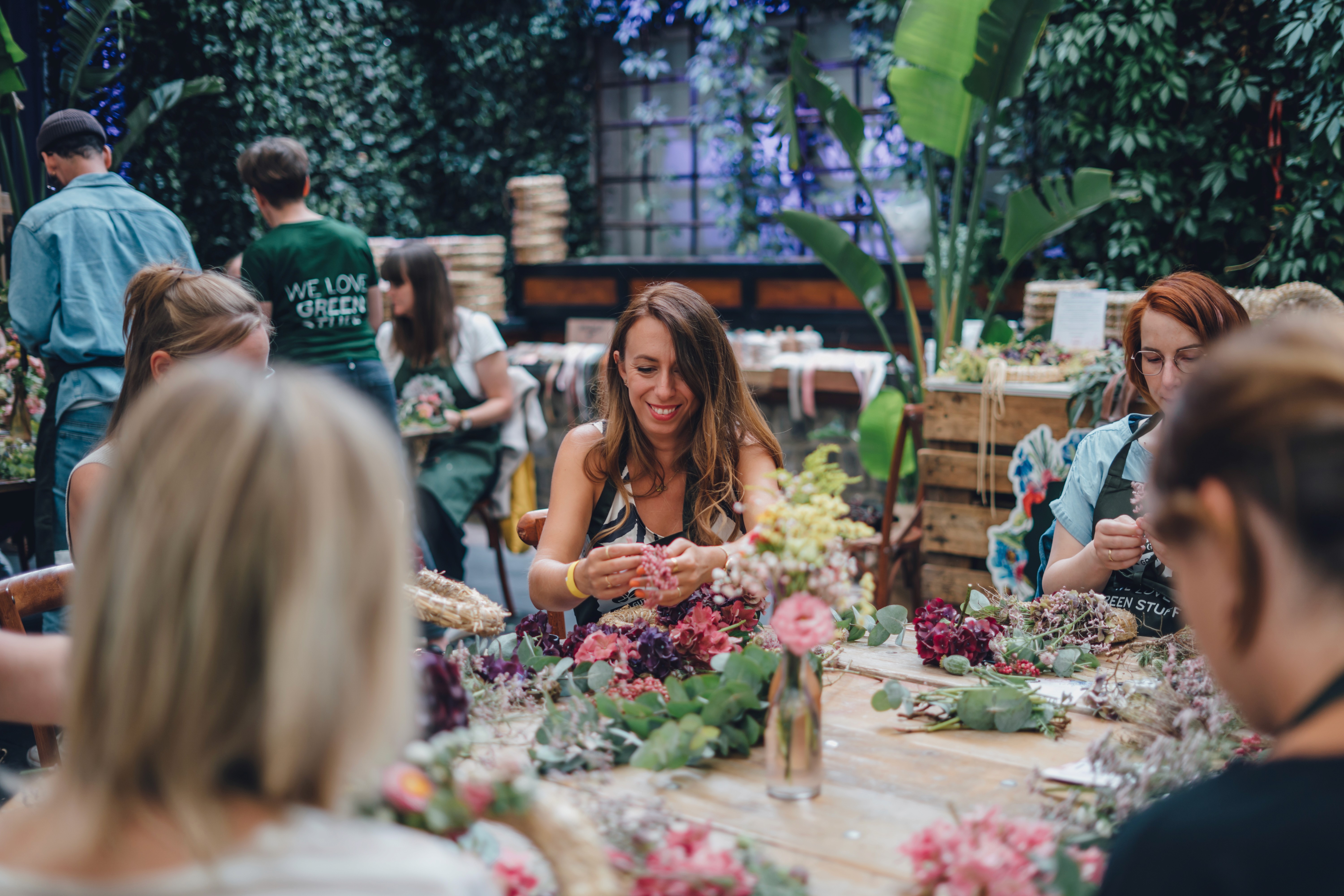 Teilnehmer:innen im Workshop 1000 gute Gründe für Blumen und Pflanzen gestalten gemeinsam an einem großen Tisch BLumen Arrangements