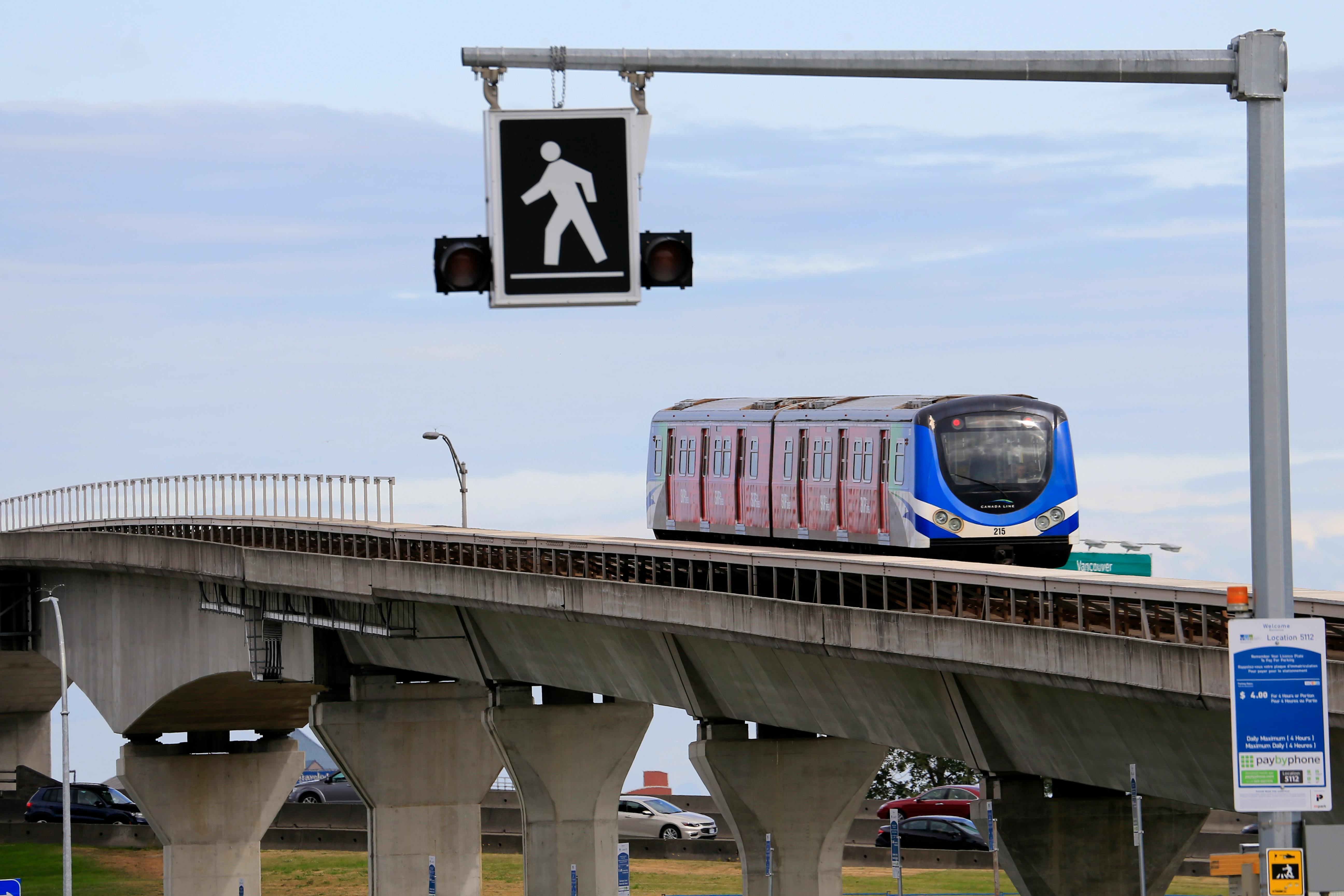 Vancouver TransLink Canada Line automated SkyTrain traveling on an elevated concrete guide way passing a large pedestrian crossing signal.