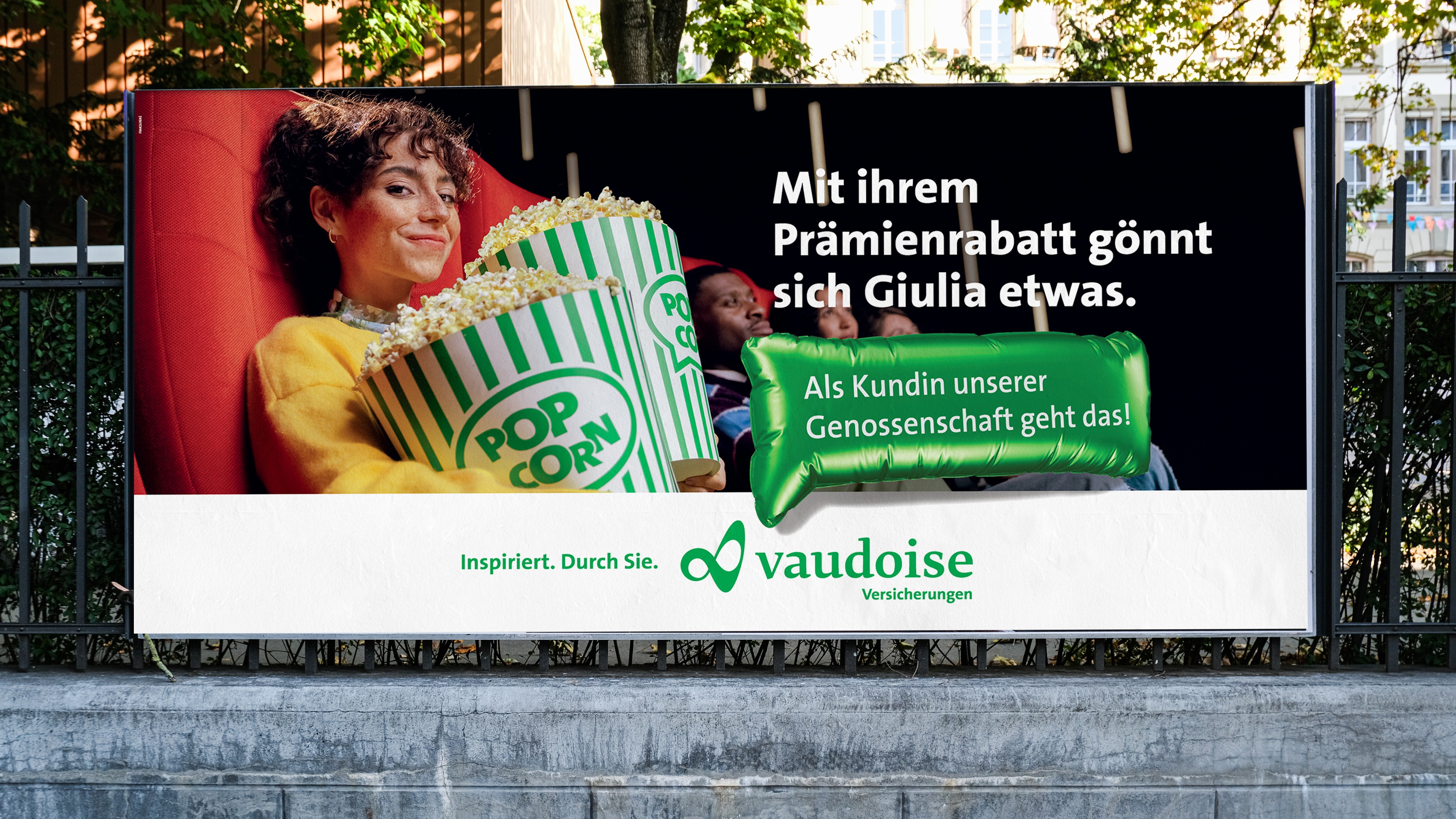 Billboard of a woman in a cinema seat holding popcorn, with German text about Vaudoise Versicherungen insurance discounts.