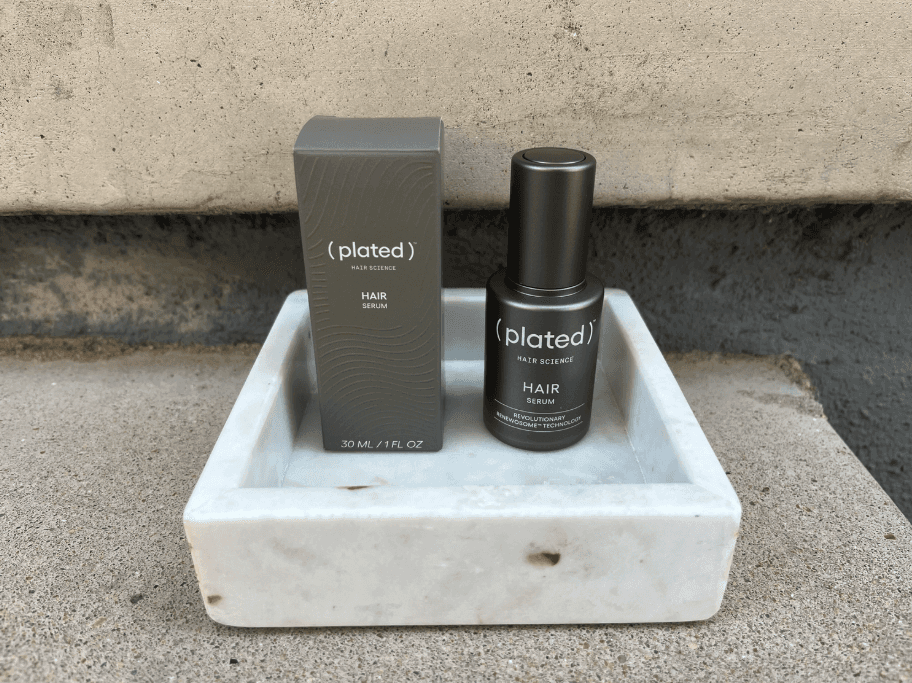 Plated Hair Science Serum sitting in a marble dish with box and bottle outside against concrete