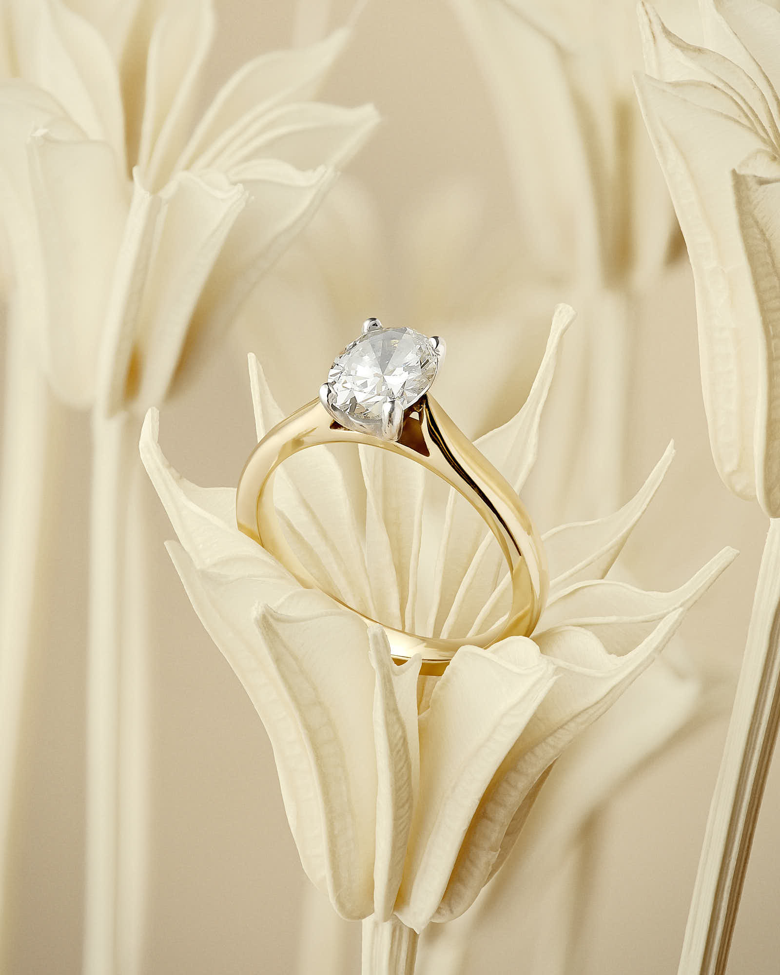Gold engagement ring with diamond on beige floral background.