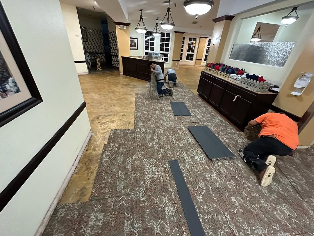 Installer laying new carpet tile across a dining hall floor