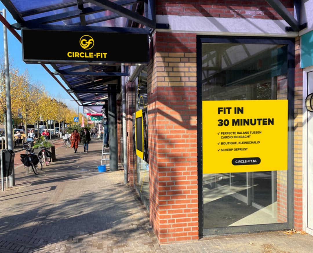 A Circle Fit hub with a large yellow sign displaying promotional text, set in an urban environment.