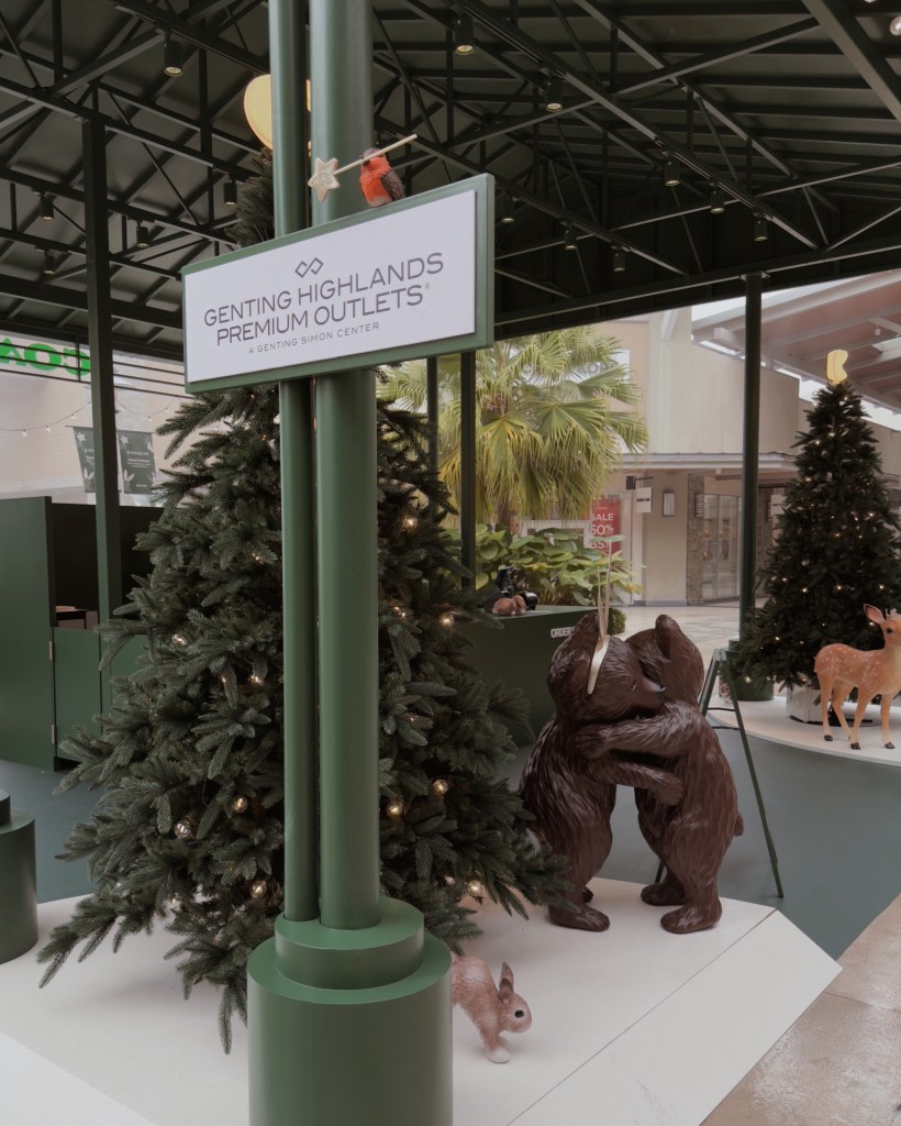A festive display at the Genting Highlands Premium Outlets featuring a sign, decorated Christmas trees, and whimsical animal sculptures like bears and a rabbit, creating a holiday atmosphere.