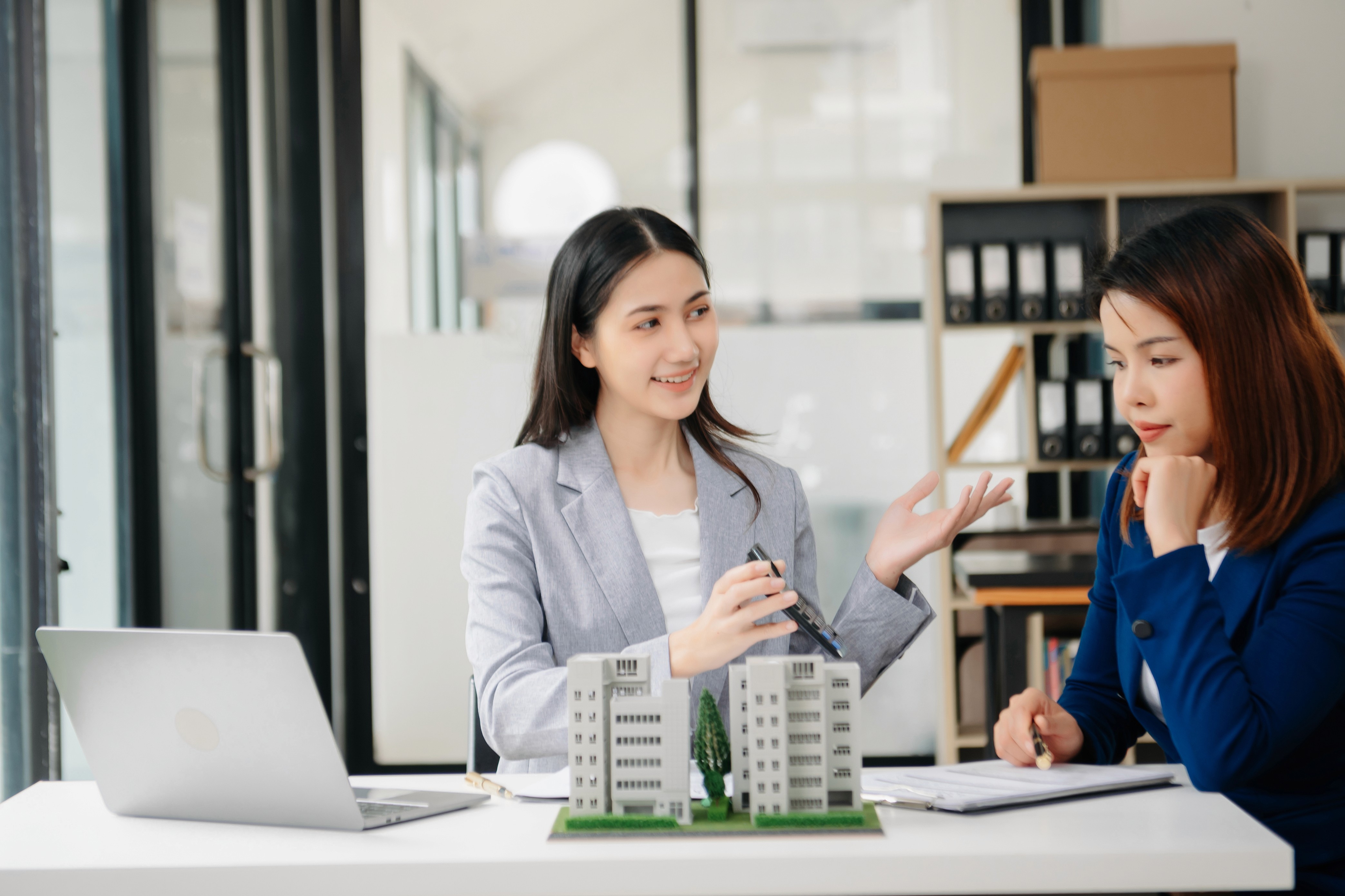 Female real estate agents discussing a model high-rise building, representing property development and investment consulting in Phnom Penh.