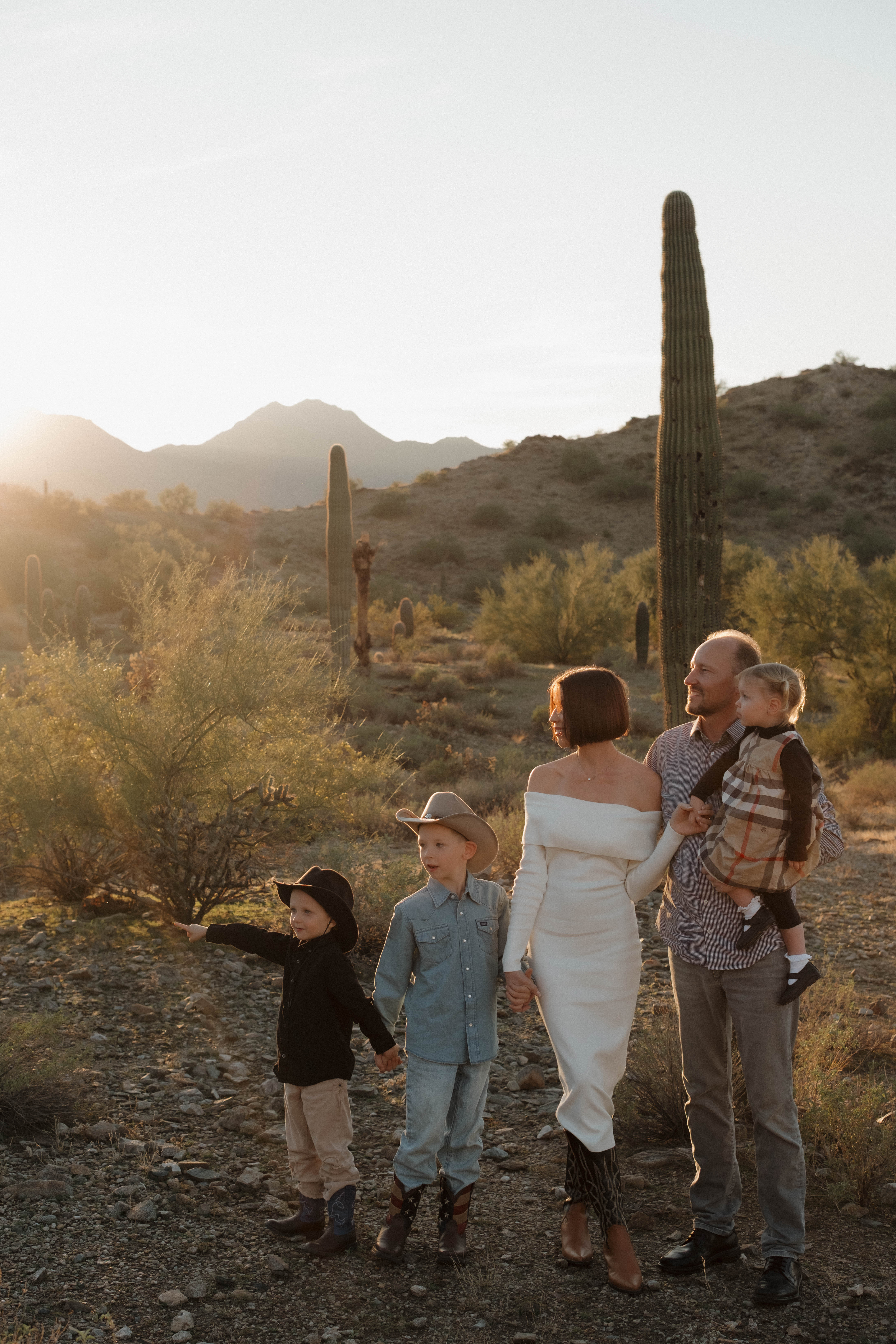 Smiling teenage boy in a white shirt and black pants standing in the Arizona desert at sunset with saguaro cacti and mountains in the background.