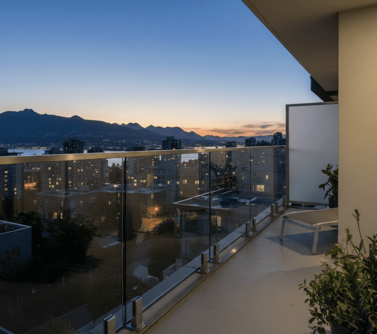 Frameless glass railing with no posts, no top rail, no frames of any kind on compact Vancouver townhouse balcony, crystal clear 12mm glass panels floating above base shoe mounts, completely unobstructed view, shared wall with neighbouring unit on right, evening atmosphere