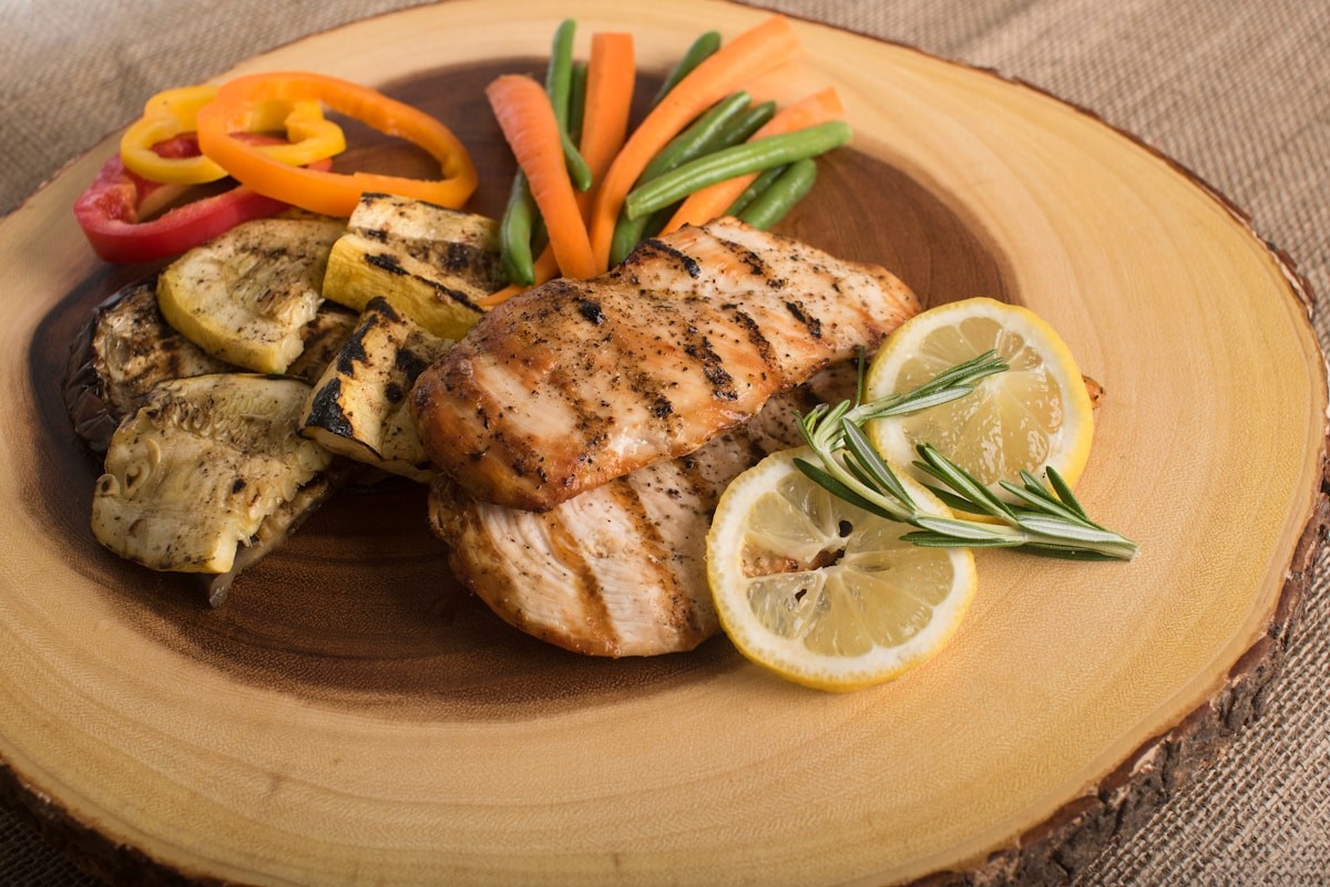 A wooden plate of grilled protein with lemon, roasted vegetables, and fresh peppers, an example of a high-protein meal for muscle preservation