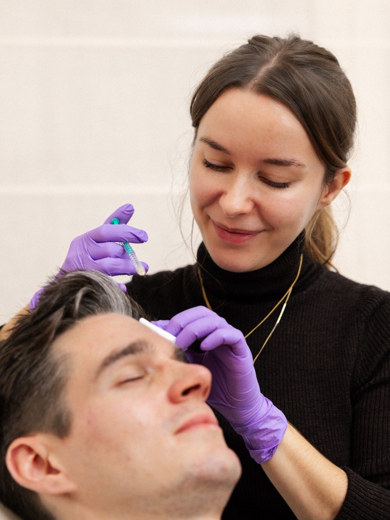 Dr. Louise Cuveele, wearing purple medical gloves, carefully administering a Botox injection to a patient at her boutique clinic.