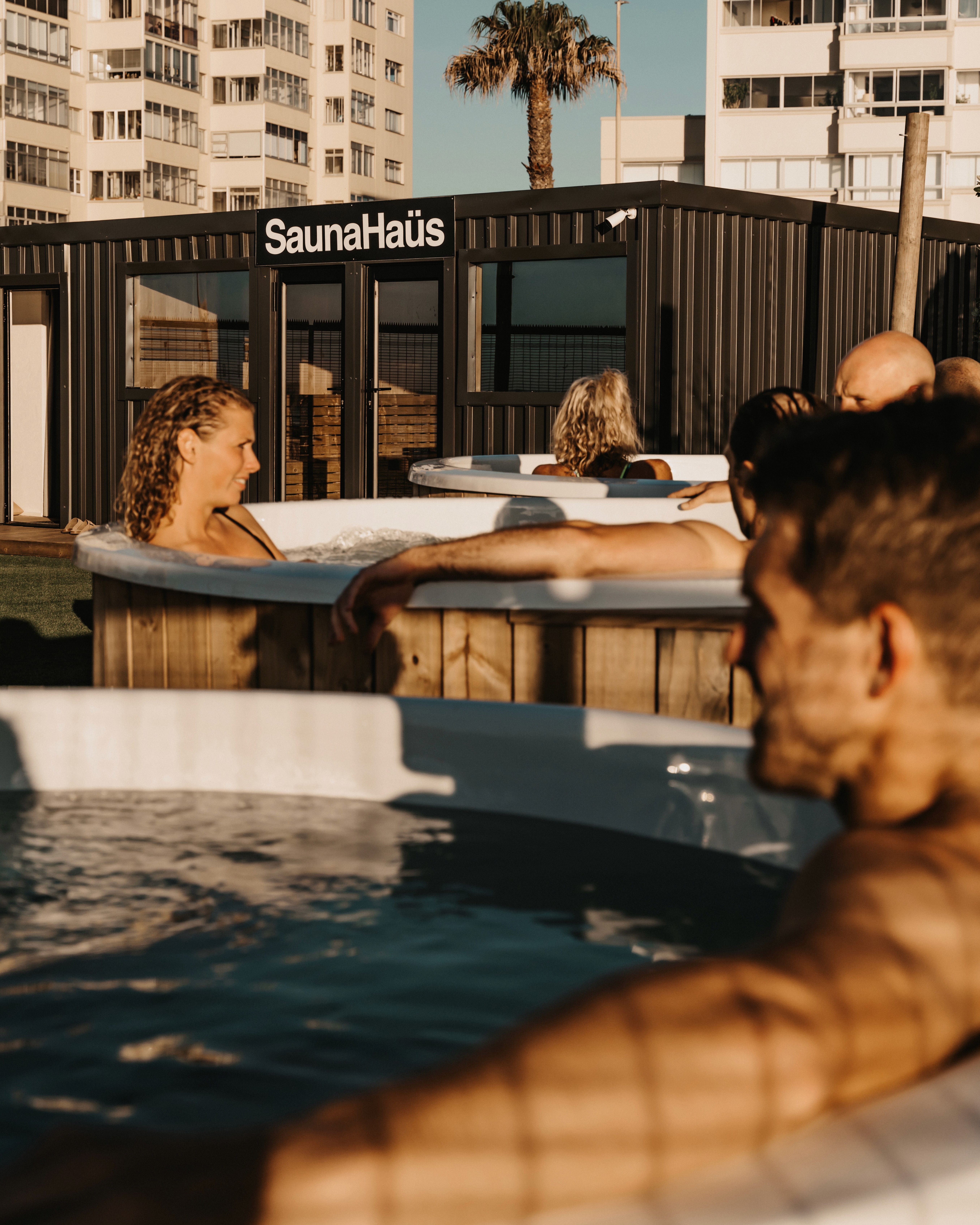 Guests relaxing in the cold plunge at SaunaHaüs Cape Town, with the sauna and Sea Point buildings in the background.