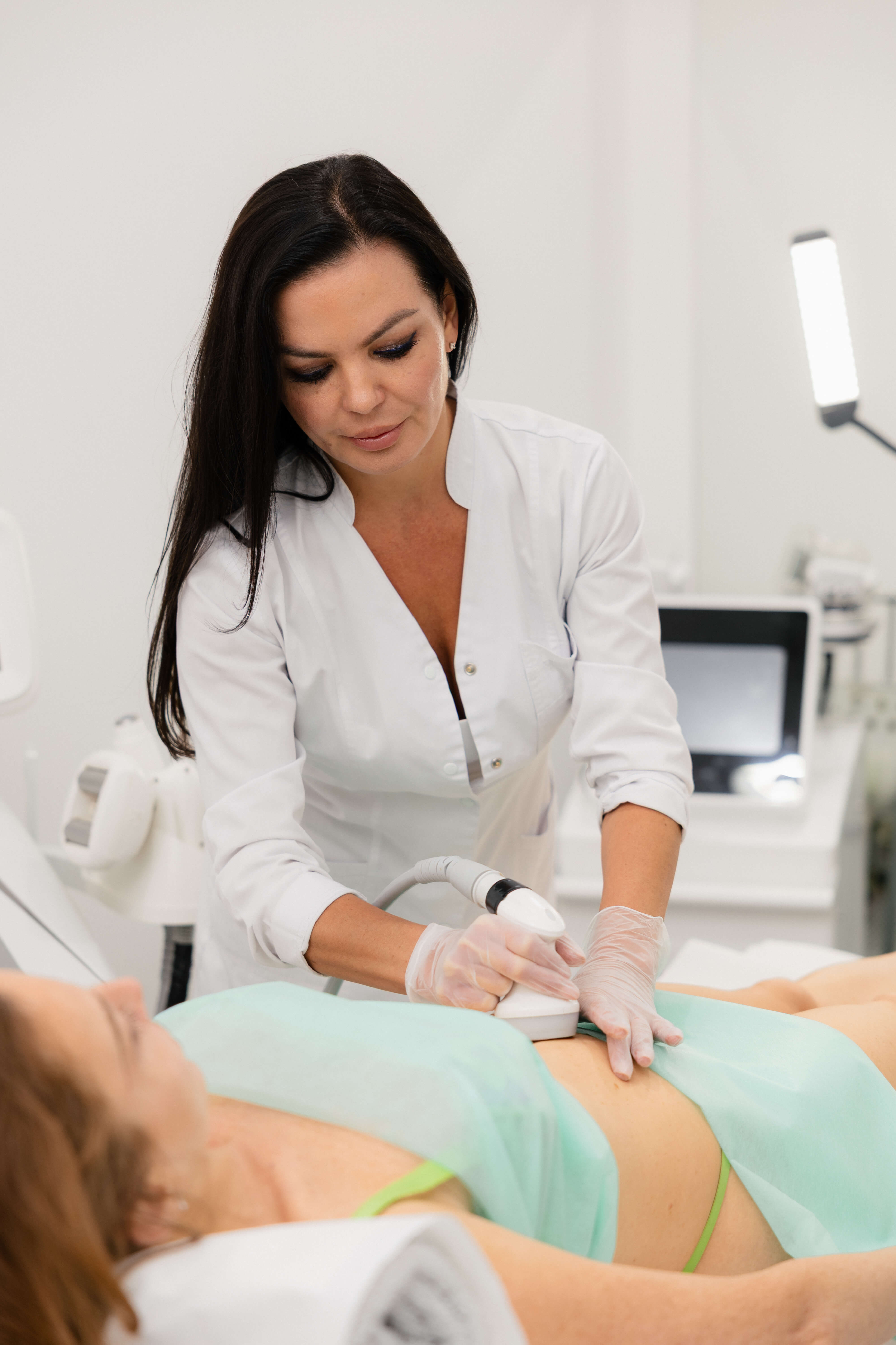 Aesthetic practitioner performing a body treatment on a client using professional clinic equipment.