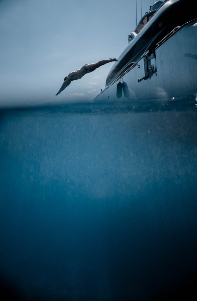 Split-level frame of a guest diving from a superyacht side deck into deep blue water, Aegean Sea, TERAMOK production