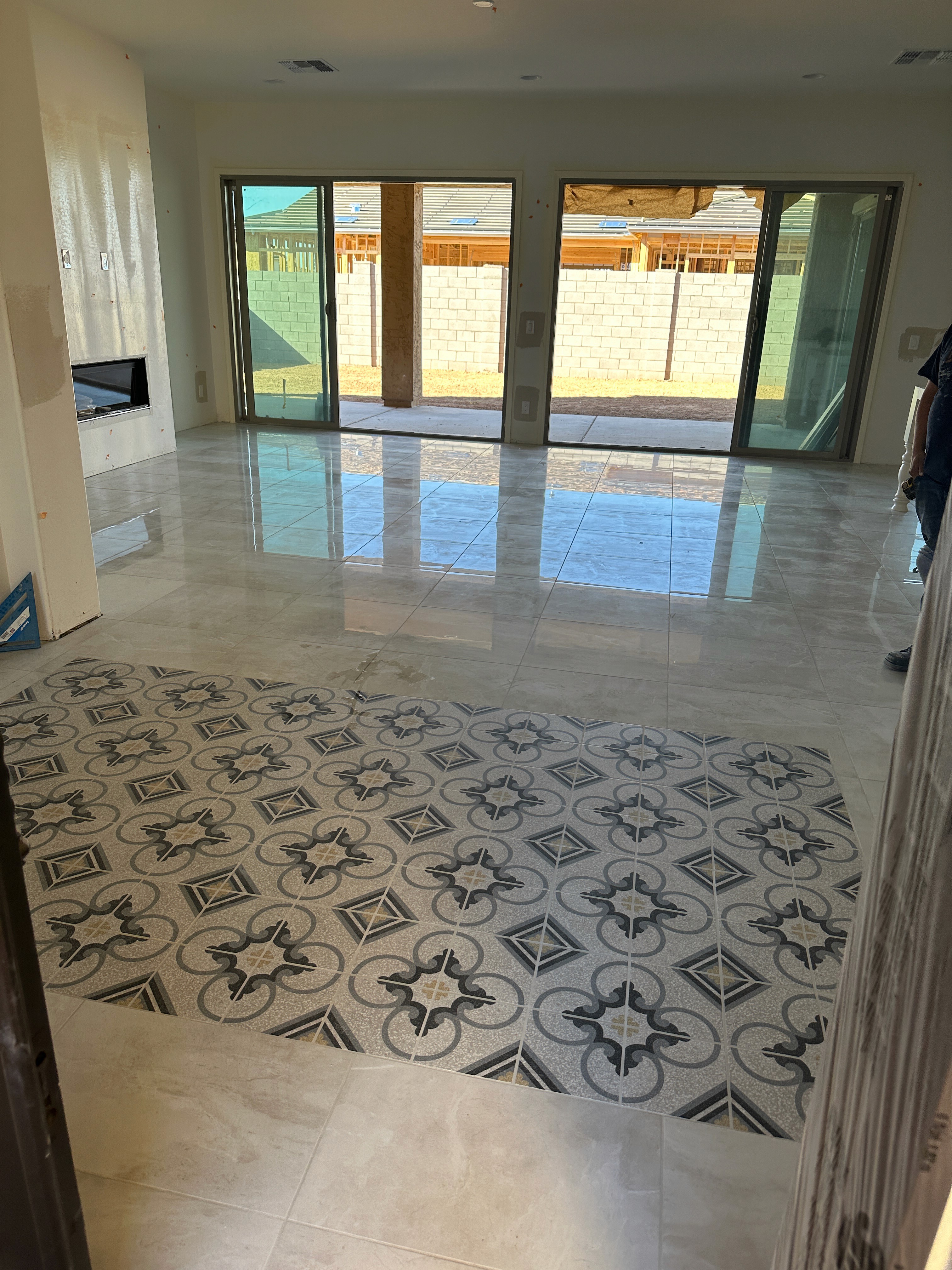 Modern living room with large sliding glass doors, fireplace, and patterned tile entryway during construction.