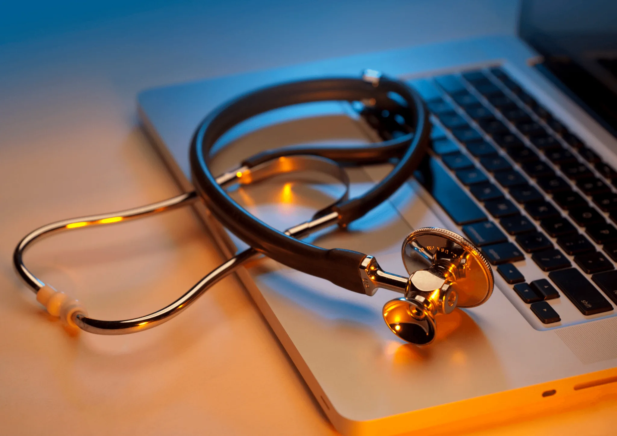 Close up of a stethoscope laying on the keyboard of a laptop.