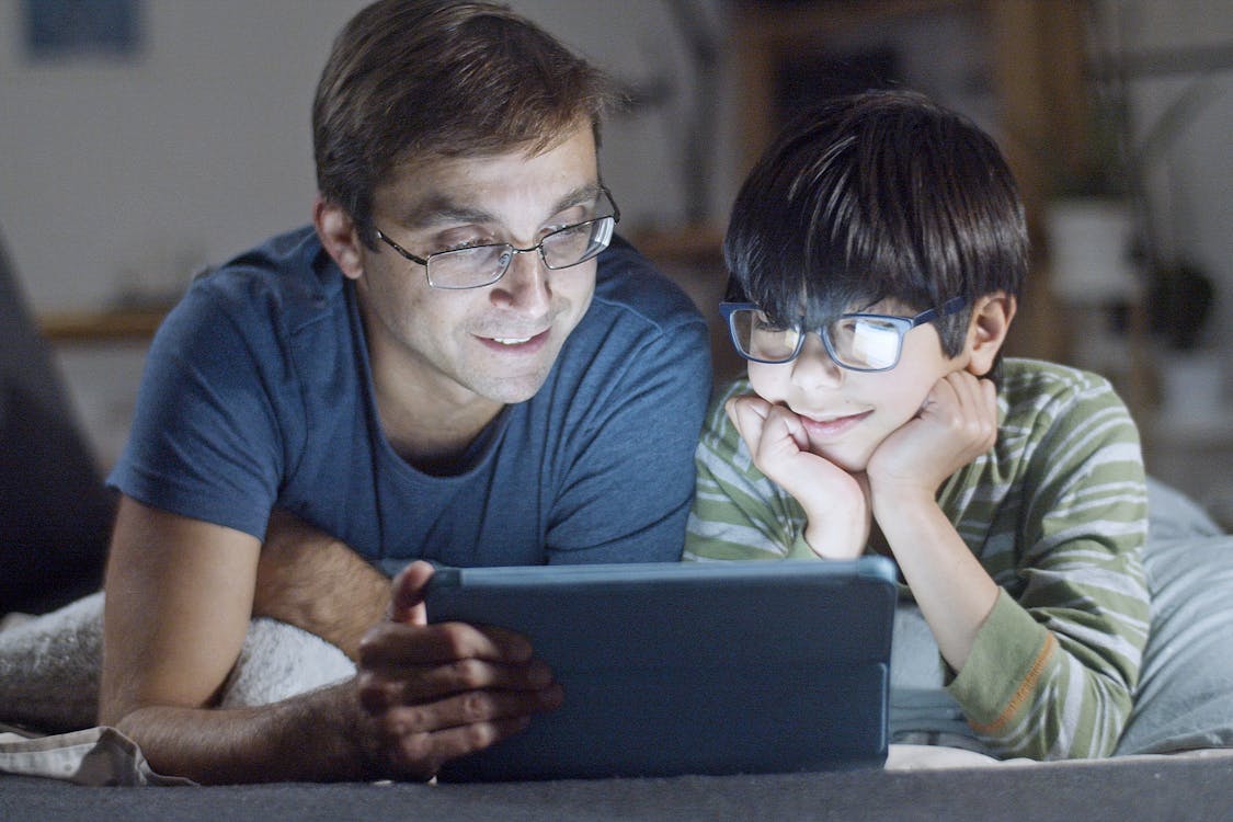 father and son watching tablet in bed together