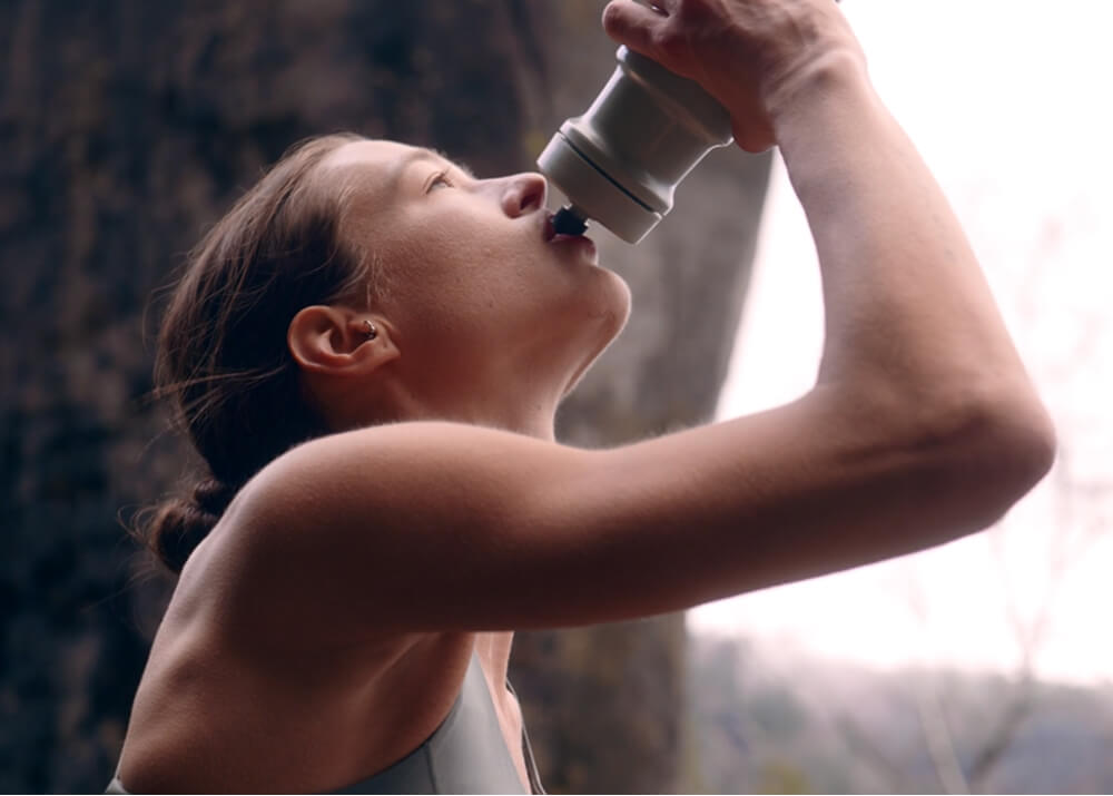 Woman drinking from a water bottle outdoors.