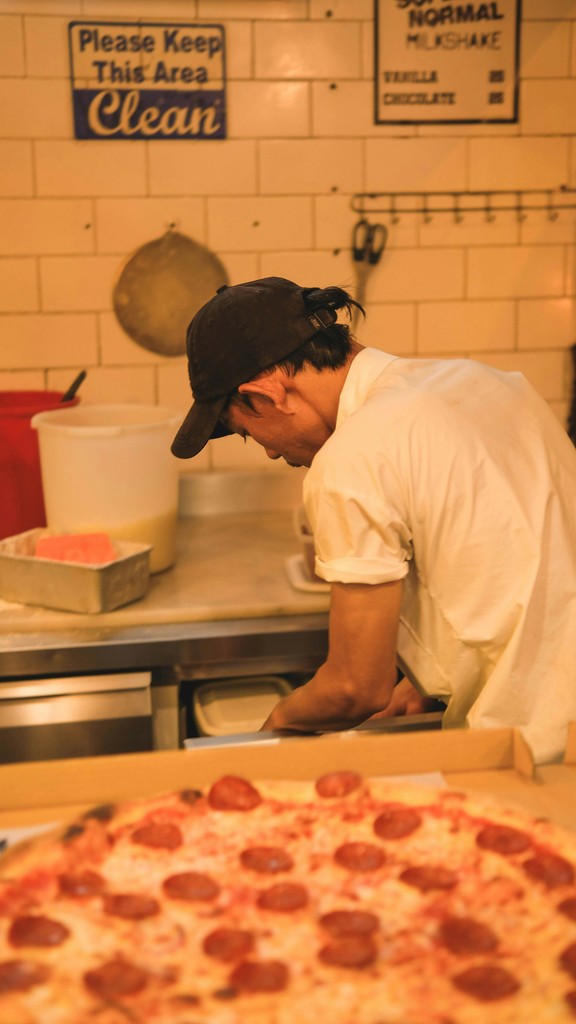 a man standing over a pizza in a kitchen