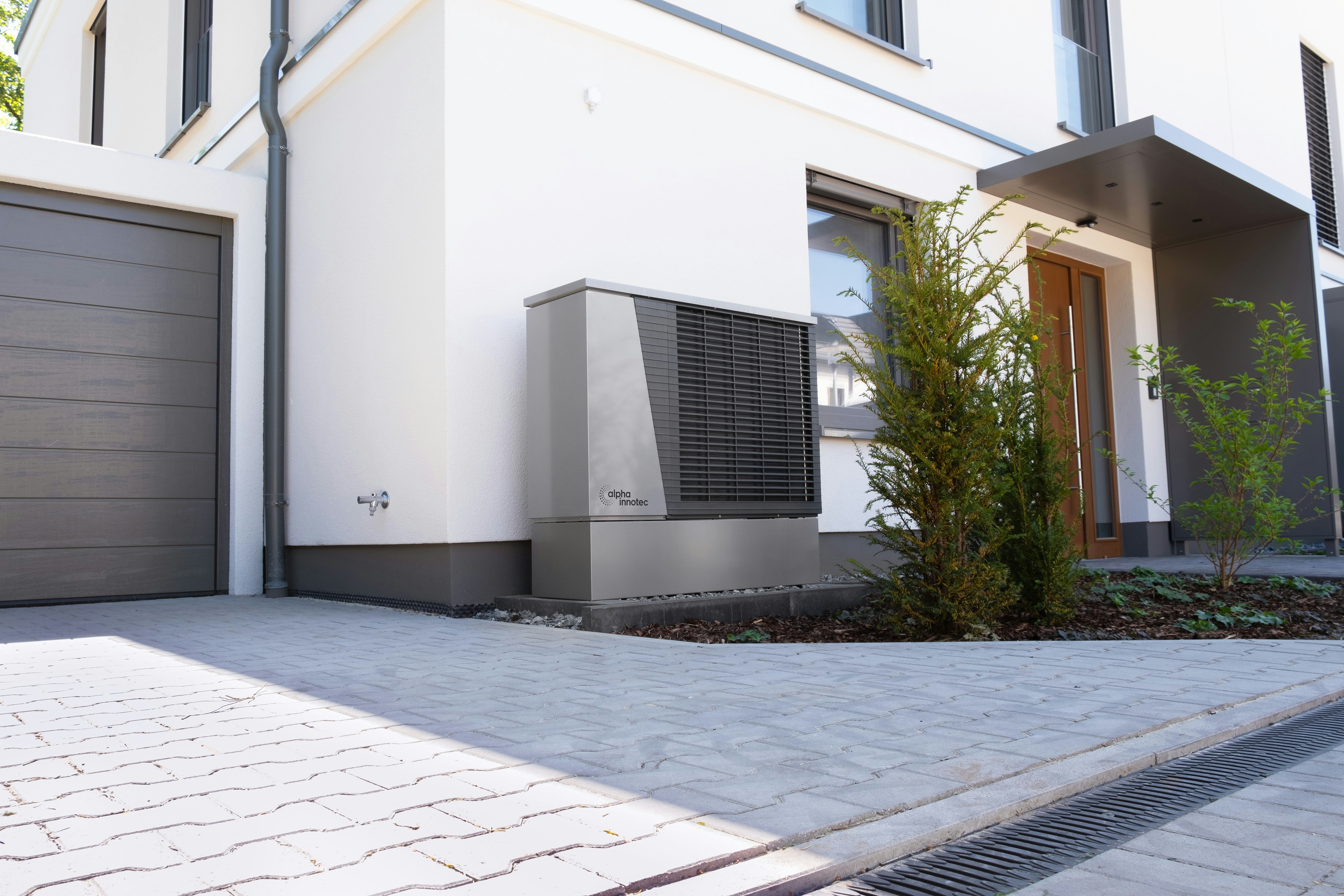 Air source heat pump installed outside a modern residential property with paved driveway and landscaped entrance.