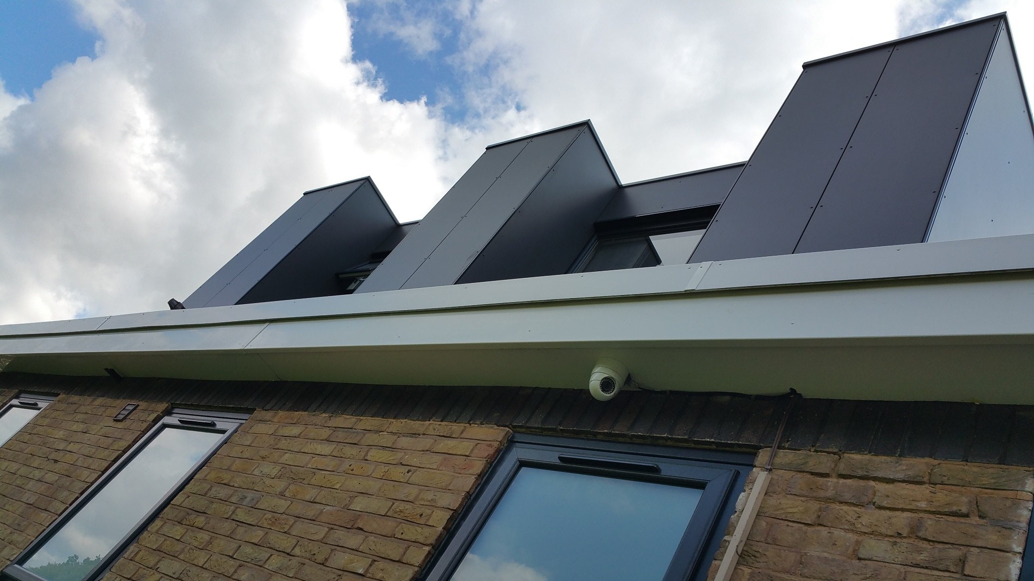 Contemporary roof pod and dormer detailing on modernised bungalow extension, finished in dark cladding against brick façade.