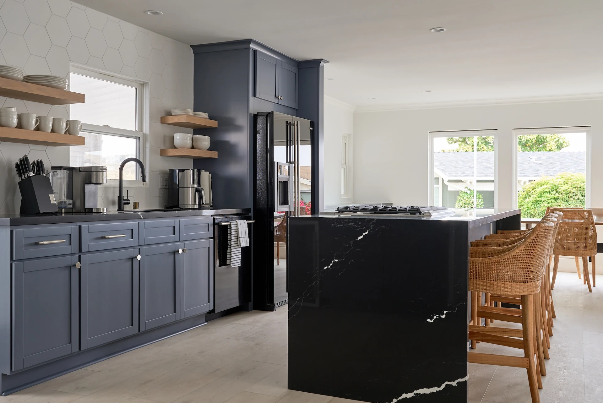 Modern kitchen with blue cabinets, black appliances, floating shelves, and a dining area . Photo by Todd Huge.