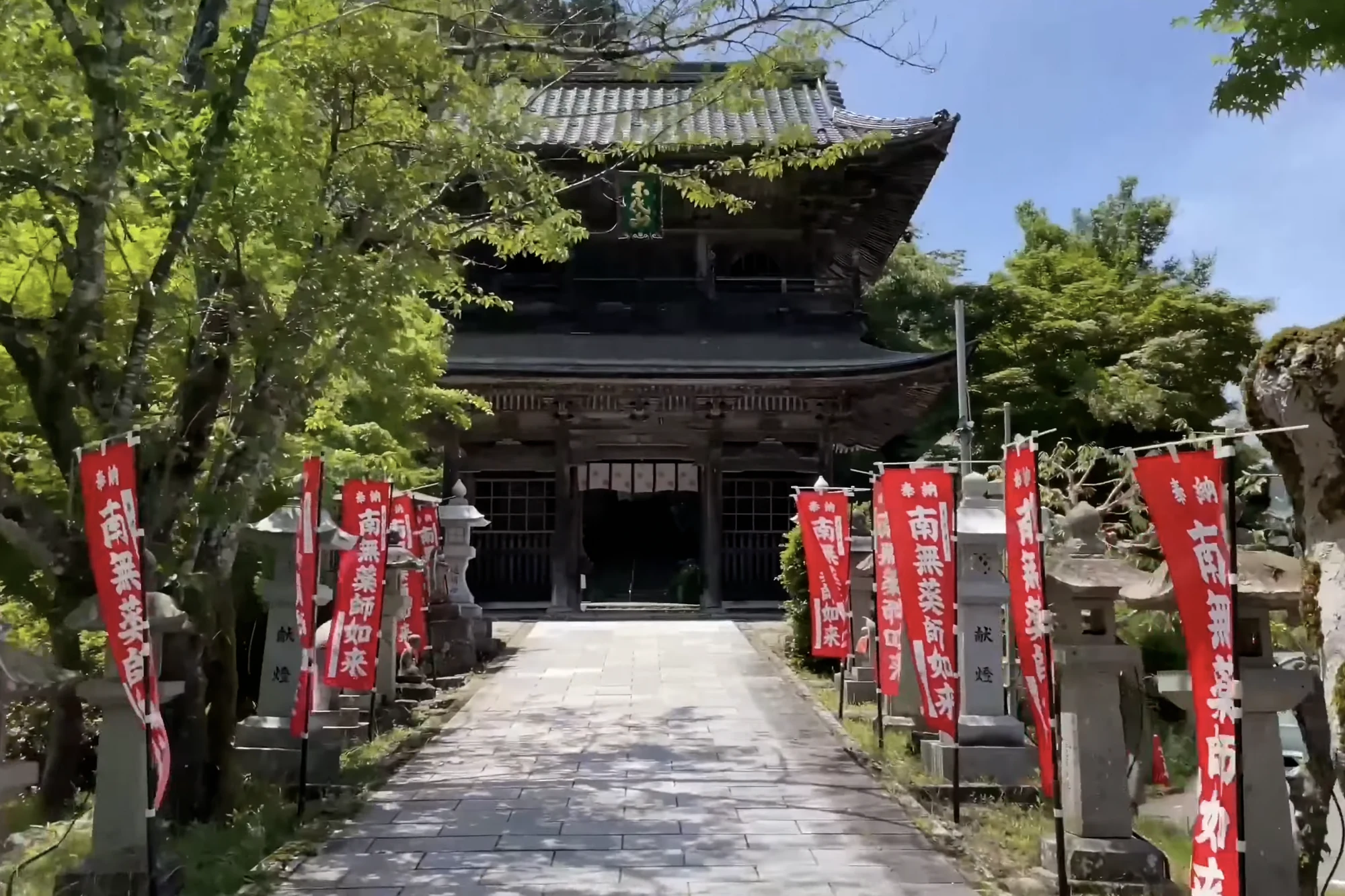 The approach to Onsenji temple above Kinosaki lined with red banners and stone lanterns.