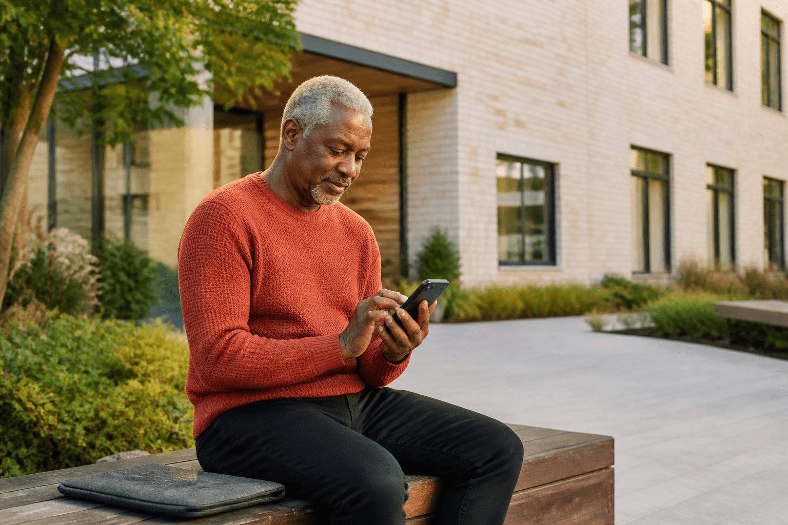 A man uses a smartphone while seated on a bench outside a building.