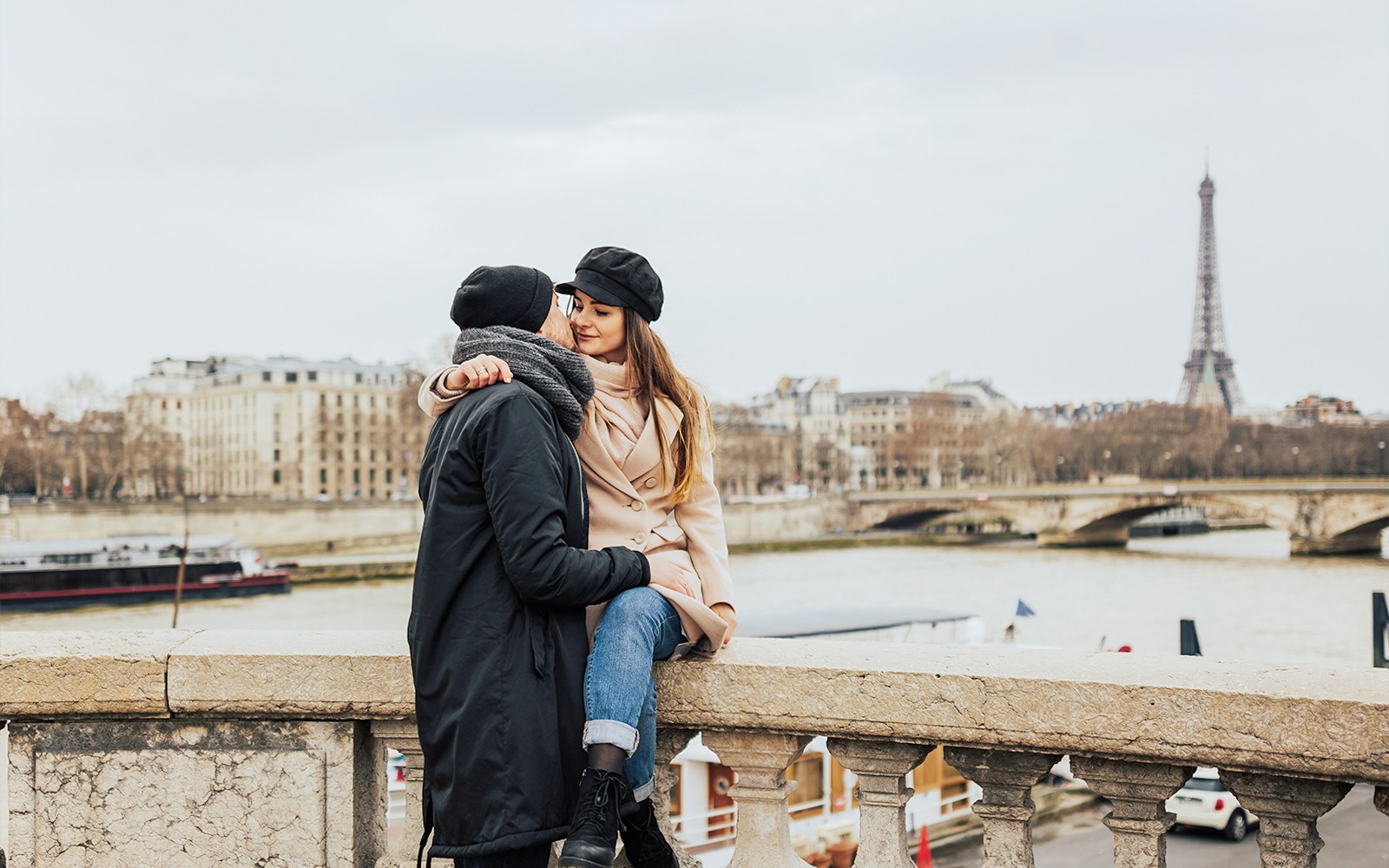 Pareja abrazándose en un puente parisino con la Torre Eiffel de fondo.