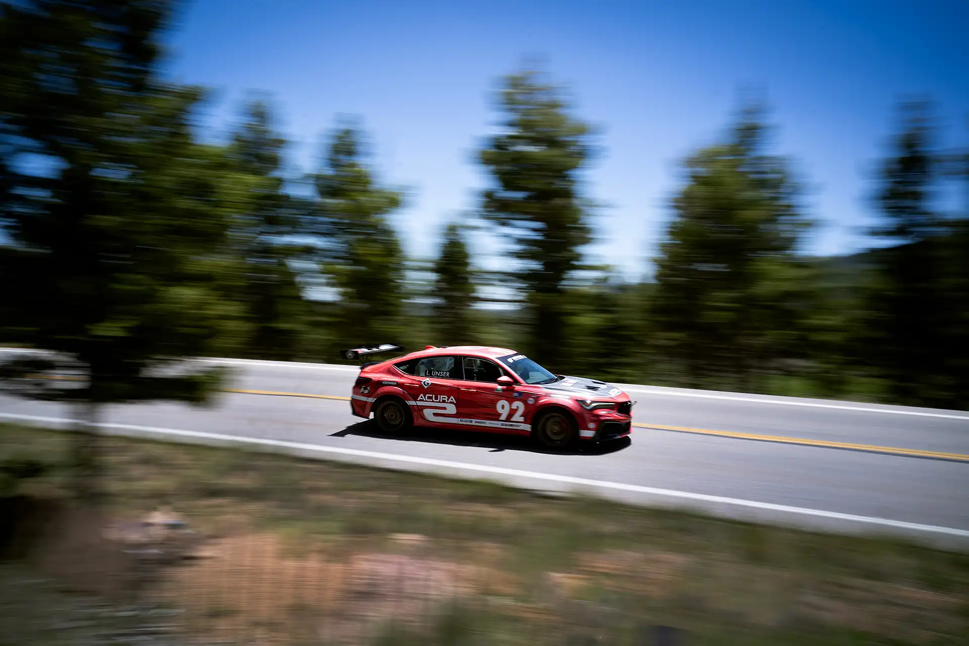 A red Acura race car speeding by on Pikes Peak mountain.