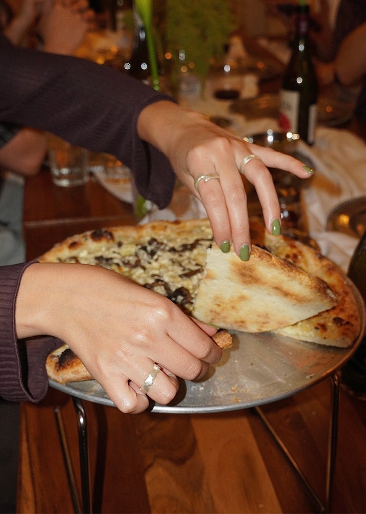 Person holding a pizza with a metal pan on a table with drinks and people in the background