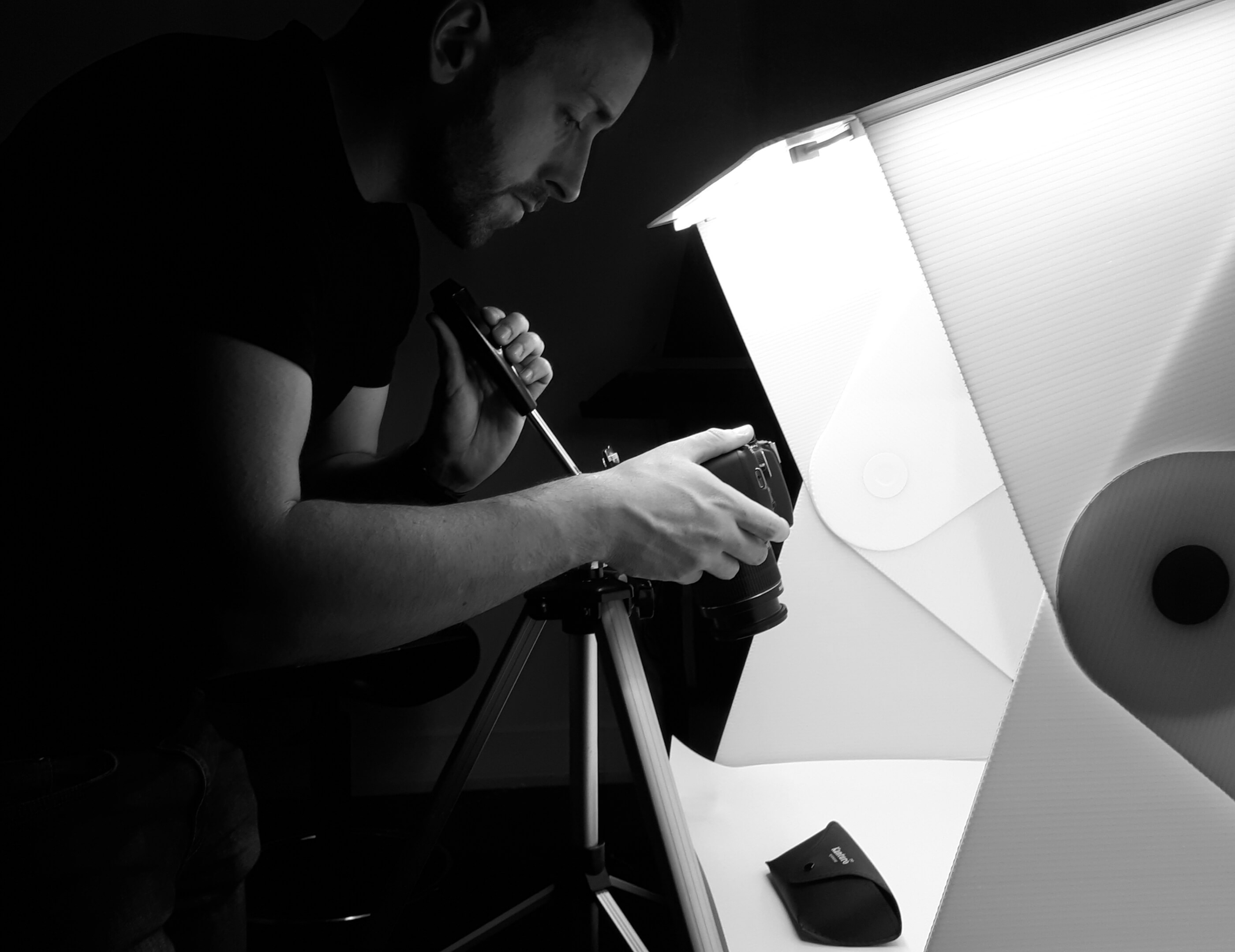 Side profile image of cormac holding a DSLR camera facing downward, taking a picture of an object placed within a lightbox